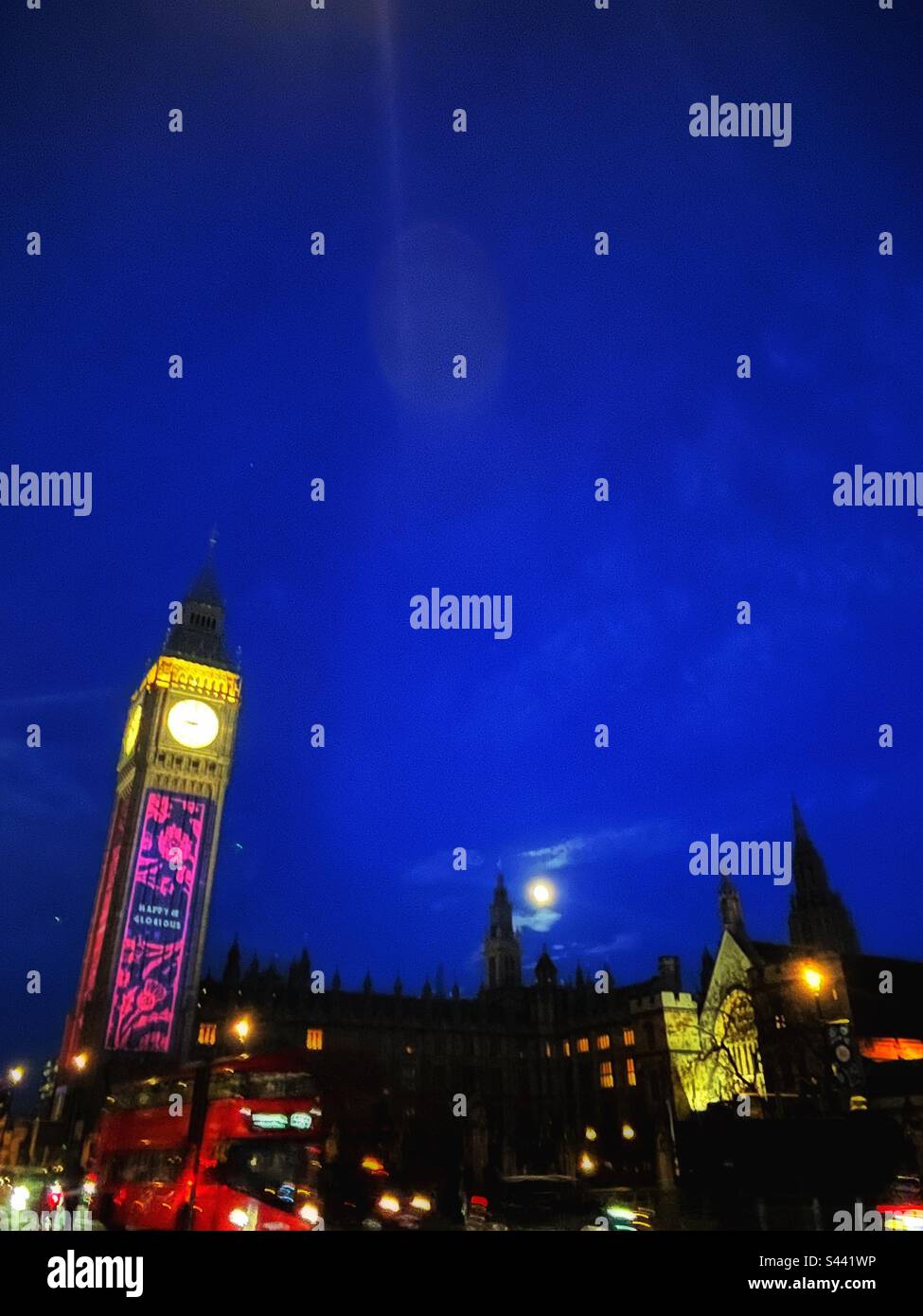Palais de Westminster, Big Ben, illustration du couronnement, bus rouge de Londres a traversé le pont de Westminster et la lune s'élève - scène animée de la ville la nuit - Image de stock capturée avec un smartphone