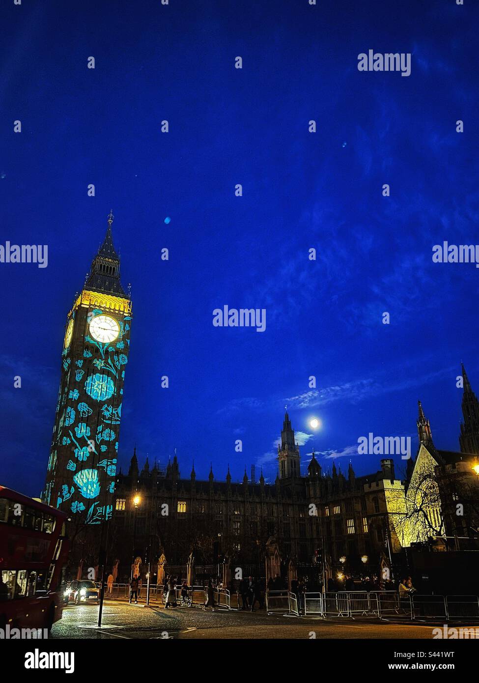 La lune s'élève au-dessus d'un Parlement illuminé à Londres, illuminé par des images de fleurs représentant les pays du Royaume-Uni célébrant le couronnement du roi Charles III - Image de stock capturée avec un smartphone
