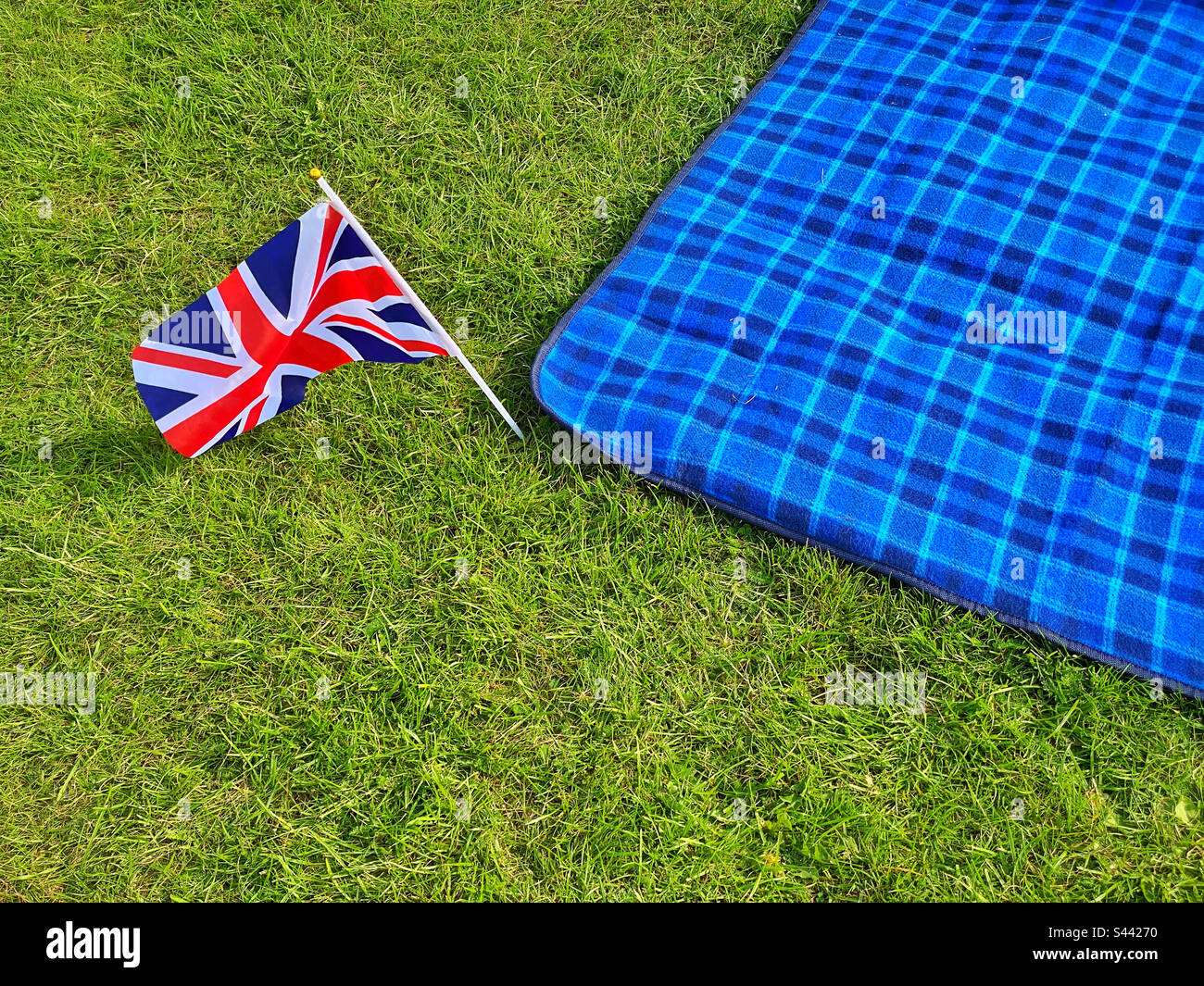 Un petit drapeau Union Jack est inséré dans le sol à côté d'une couverture bleue sur un champ d'herbe. Préparatifs de célébration initiale pour le couronnement du roi Charles III et de la reine Camila. Photo©️C. HOSKINS. Banque D'Images