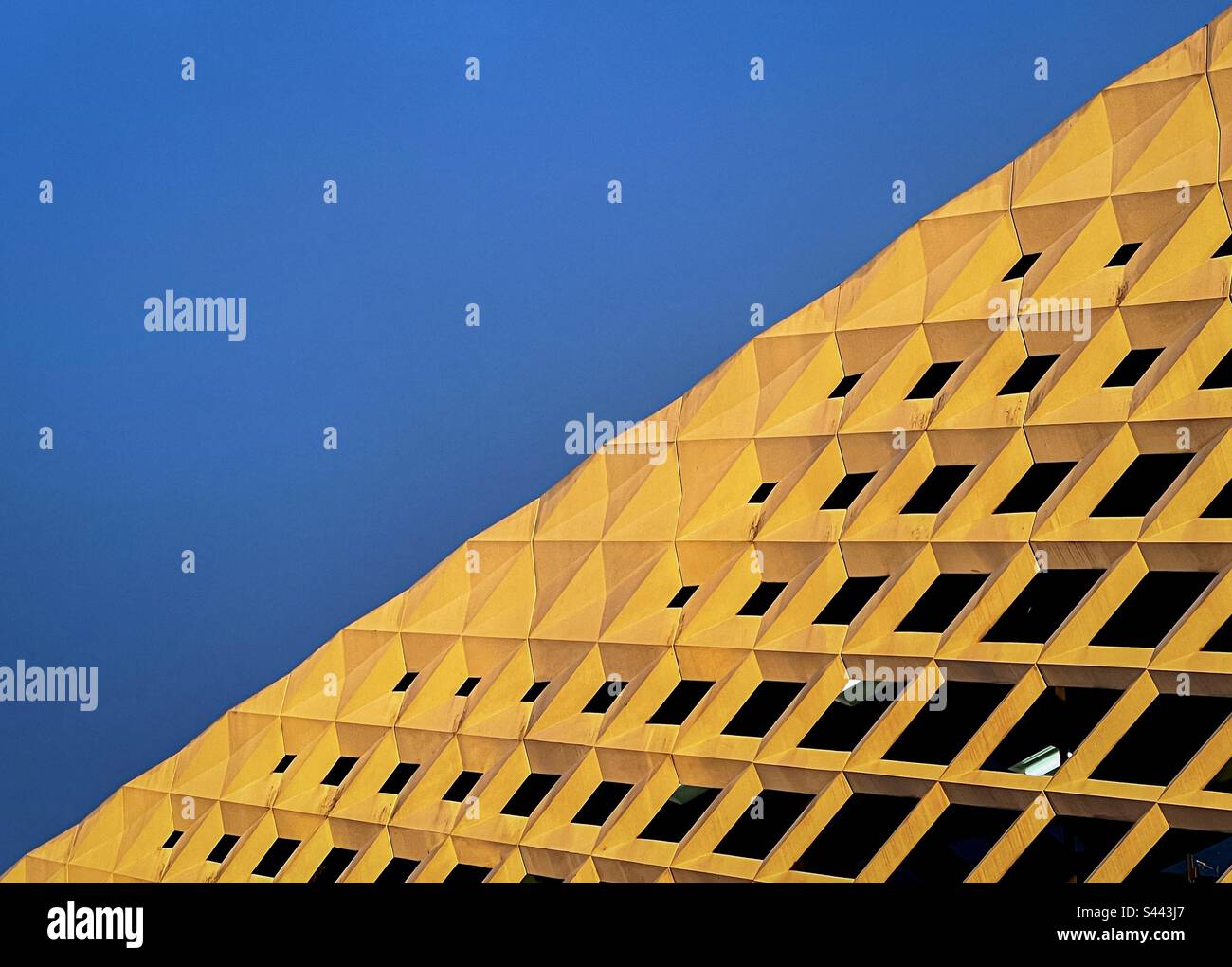 Gros plan abstrait de la façade du bâtiment avec des reflets dorés dans le soleil de la fin de l'après-midi contre le ciel bleu. Lignes et répétition. - Image de stock capturée avec un smartphone