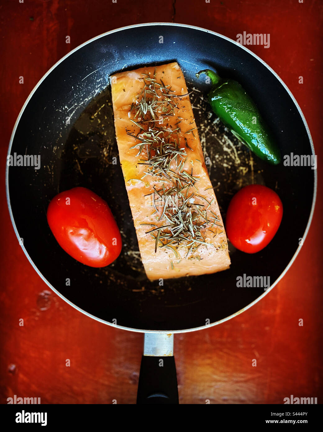 Un morceau de saumon au romarin, deux tomates rouges et un piment rouge vert chaud prêt à être grillé à Queretaro, au Mexique Banque D'Images
