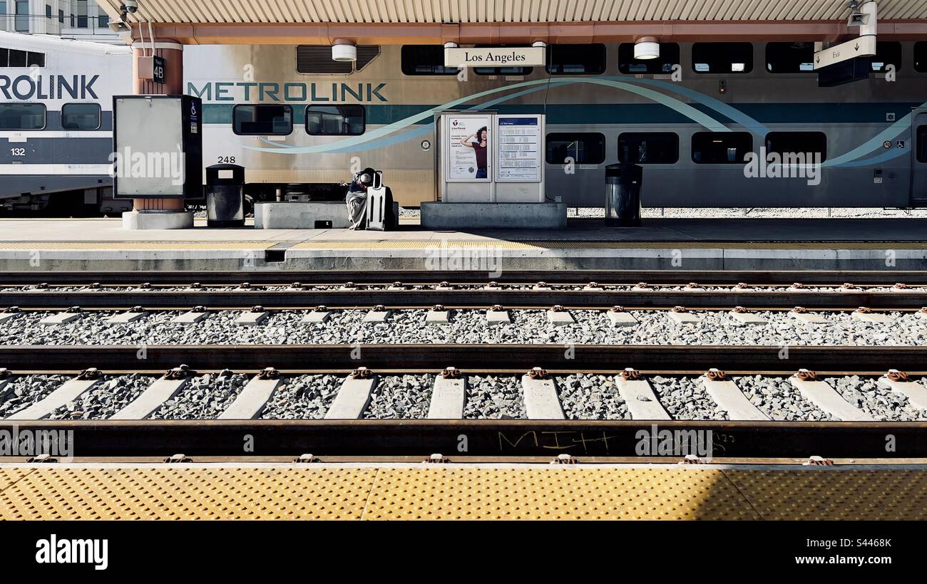 LOS ANGELES, CA, DEC 2022: Personne anonyme, regardant vers le bas en attendant avec une valise sur la plate-forme à Union Station dans le centre-ville, avec le train Metrolink derrière Banque D'Images LOS ANGELES, CA, DEC 2022: Personne anonyme, regardant vers le bas en attendant avec une valise sur la plate-forme à Union Station dans le centre-ville, avec le train Metrolink derrière Banque D'Images