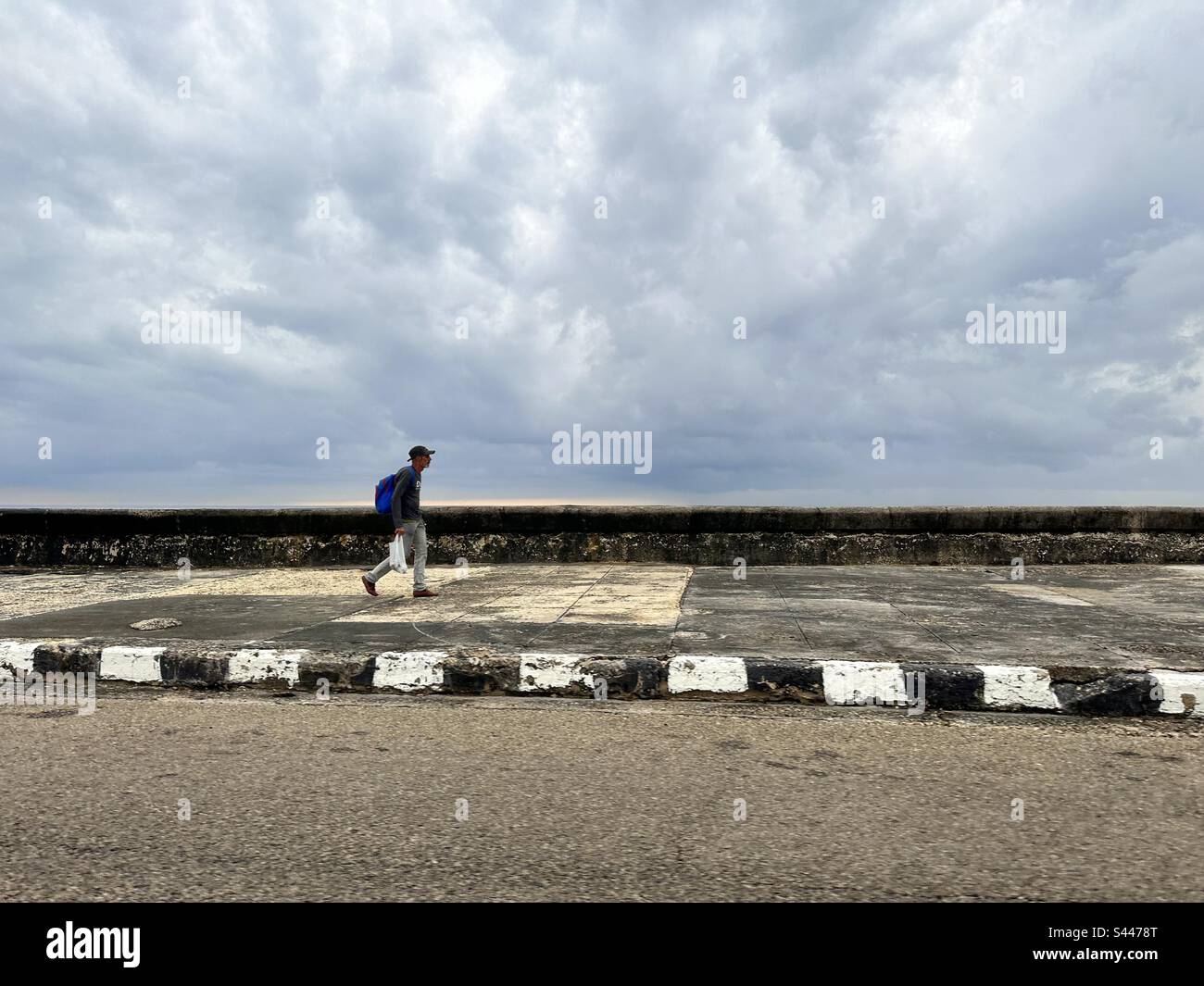 Homme marchant le long de la digue de la havane ‚el malecón dans une journée nuageux. La Havane, Cuba Banque D'Images