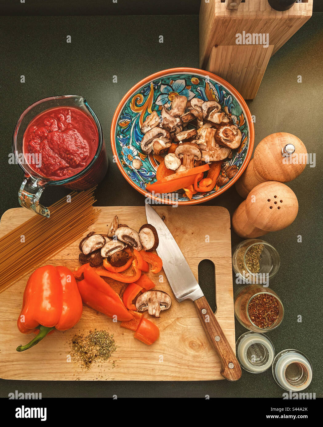 La nourriture italienne prépare les tomates en purée dans une tasse à mesurer, les champignons en tranches et les poivrons sur la planche à découper avec un couteau, un saupoudreur, un moulin à poivre, des épices, des pâtes sur le comptoir de cuisine vu d'en haut. Banque D'Images