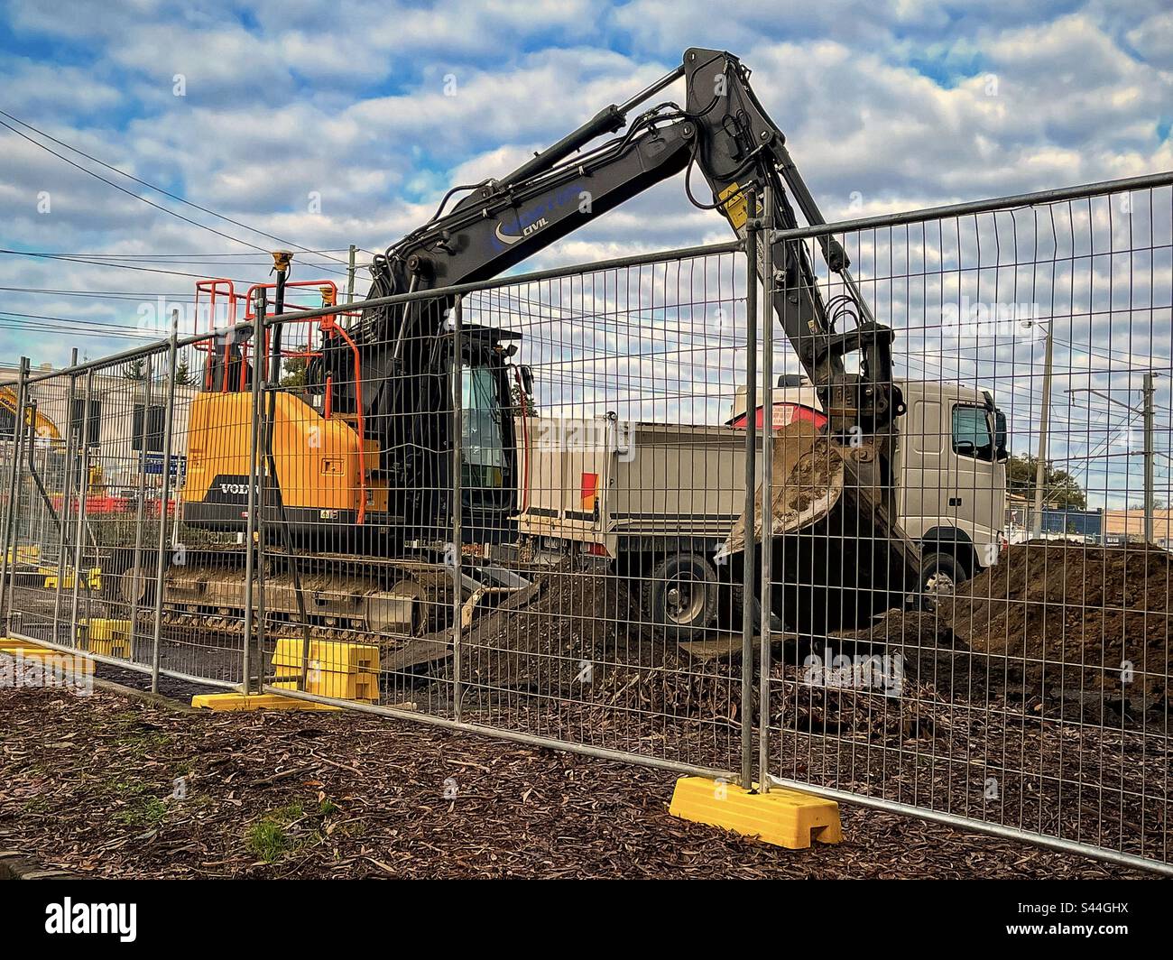 Pelle hydraulique chargeant le sol dans le camion-benne derrière la clôture de sécurité de construction sur le chantier. Banque D'Images