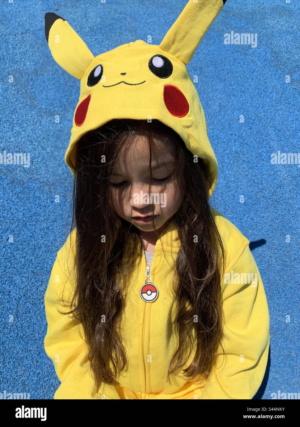 Petite fille assise sur fond bleu avec le sweat à capuche Pokémon. Banque D'Images