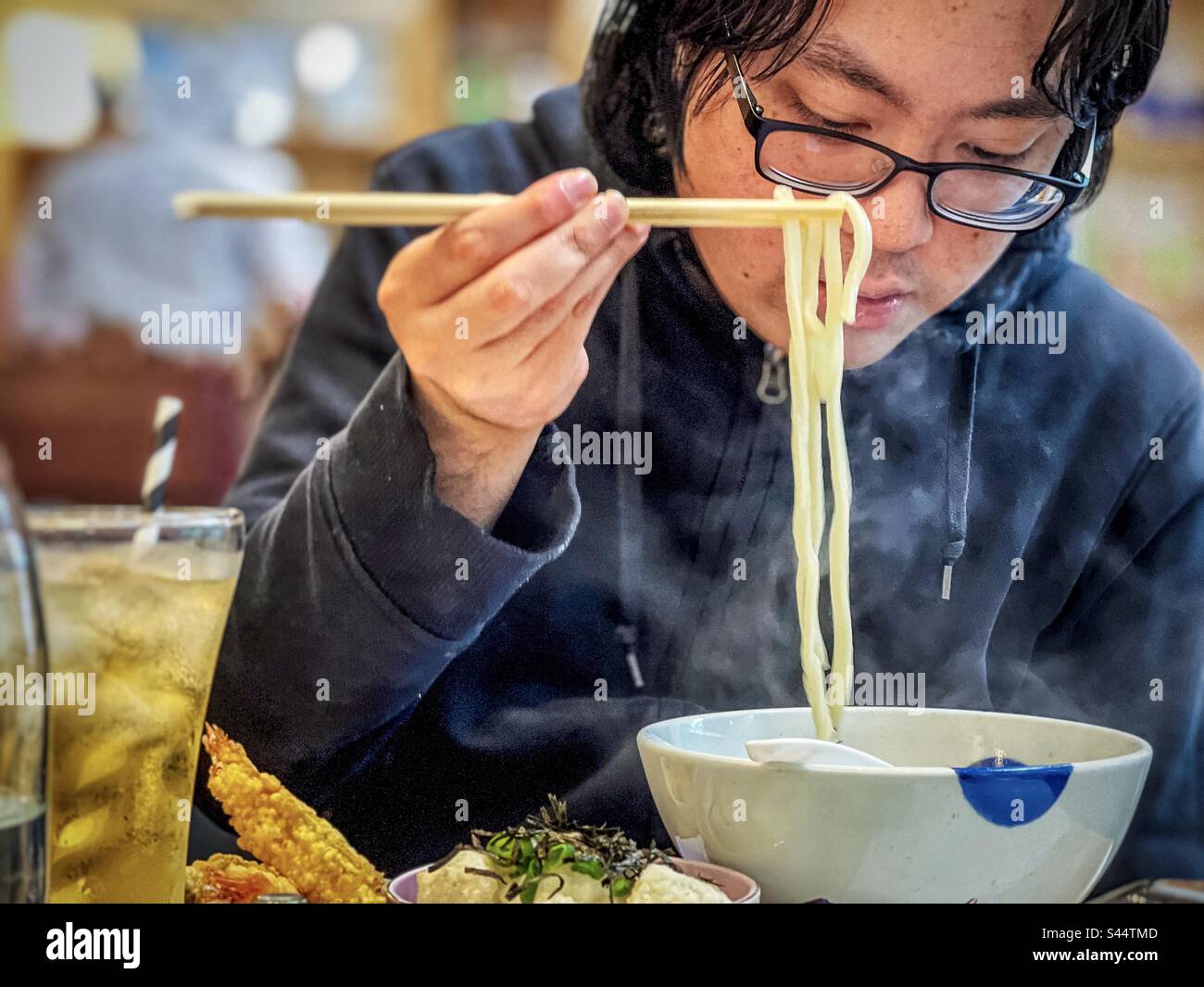 Un jeune homme asiatique appréciant un bol de soupe de nouilles udon chaudes dans un restaurant japonais. - Image de stock capturée avec un smartphone