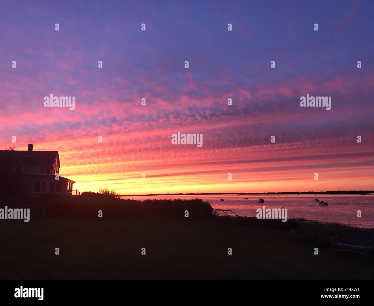 Le coucher du soleil de Cape Cod illumine le ciel et fixe une maison de plage fenêtres aglow. Banque D'Images