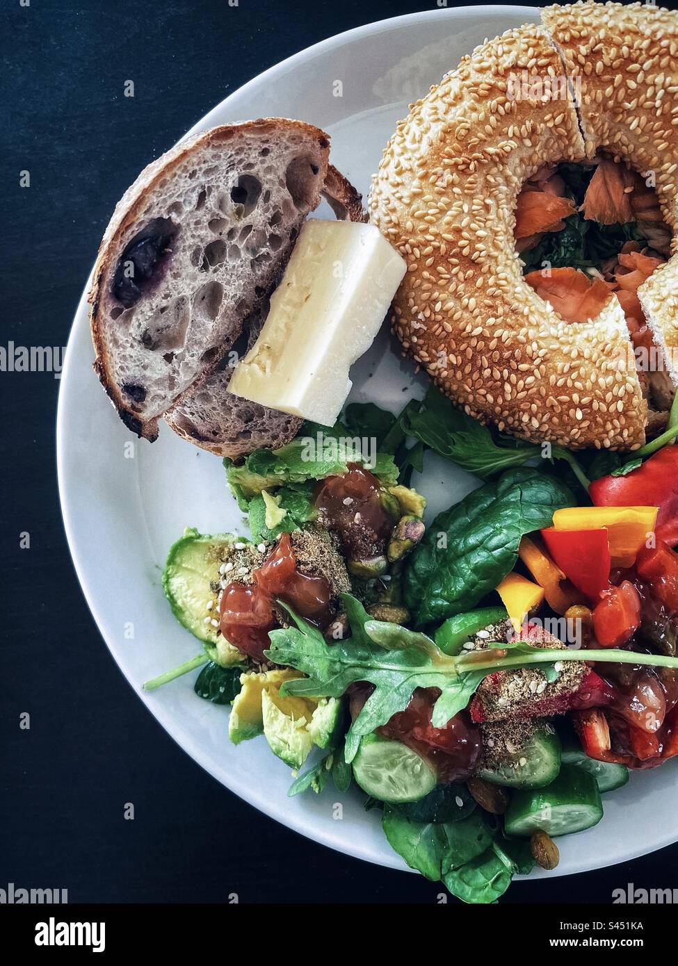 Directement au-dessus de la vue de bagel de saumon, levain d'olive avec fromage et salade fraîche, tranches d'avocat sur plaque blanche sur table noire. Mangez vos couleurs. Une alimentation saine. Banque D'Images