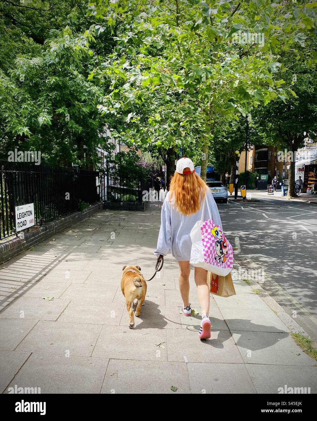 Une femme aux cheveux roux promène son bouledogue le long de la rue à Londres - Image de stock capturée avec un smartphone