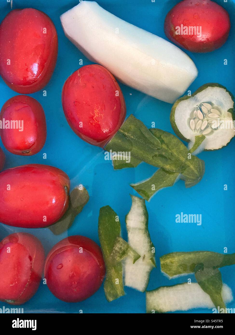 Vue rapprochée des tomates biologiques et du concombre en plastique bleu recipiente avec de l'eau Banque D'Images