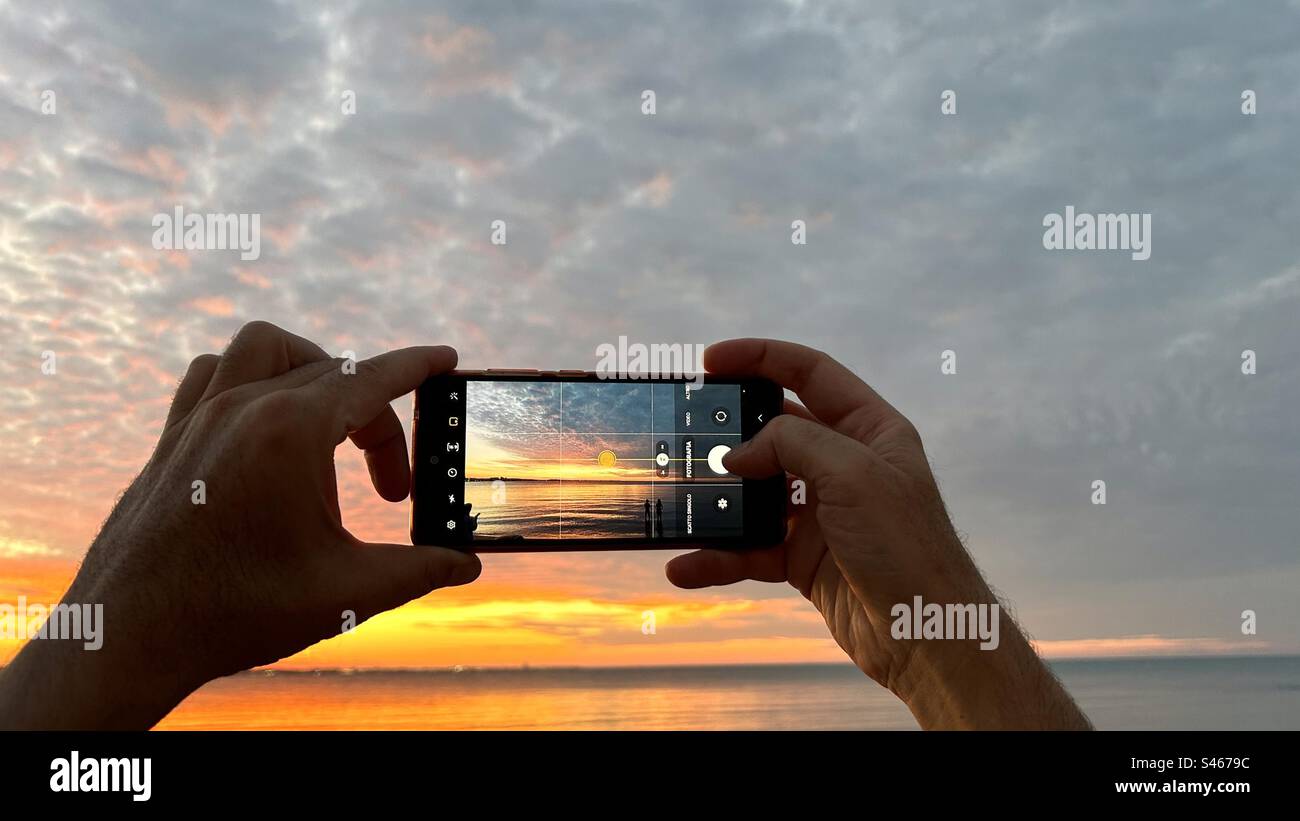 Les mains masculines tiennent un téléphone portable tout en prenant une photo d'un beau coucher de soleil d'été Banque D'Images