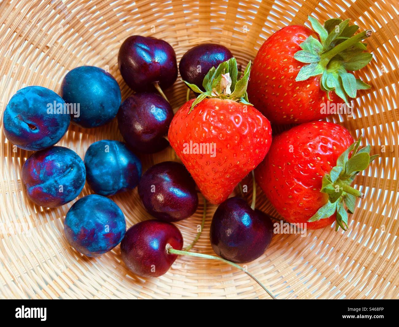 Trois fraises, quelques prunes et cerises dans un panier en osier. Frais, coloré, juteux, sucré, nutritif, fruits d'été. - Image de stock capturée avec un smartphone