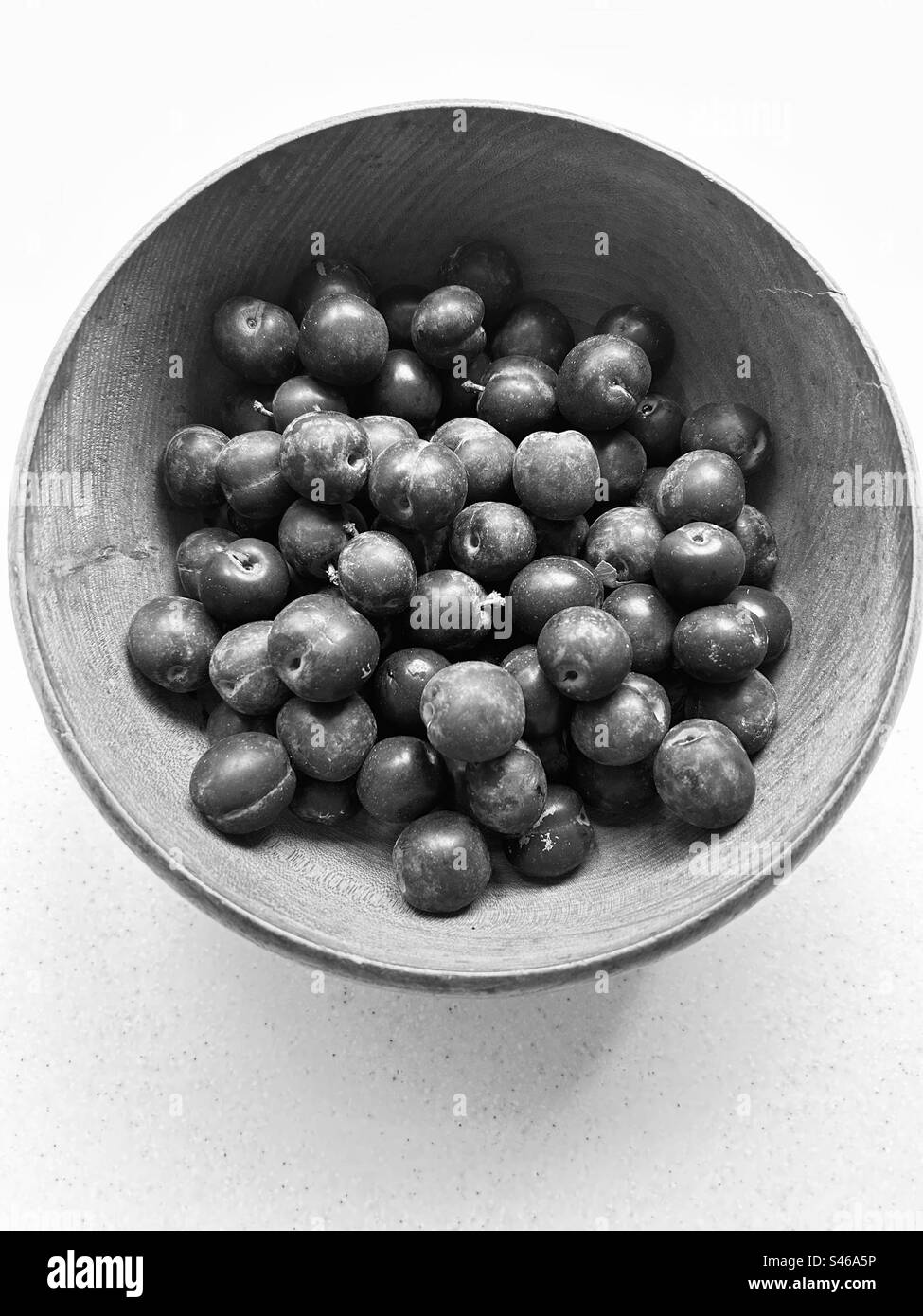 Prunes monochromes dans un bol en bois grainé.bleu violacé. Fouillé hier dans le verger de la communauté locale. Frais et juteux. Banque D'Images
