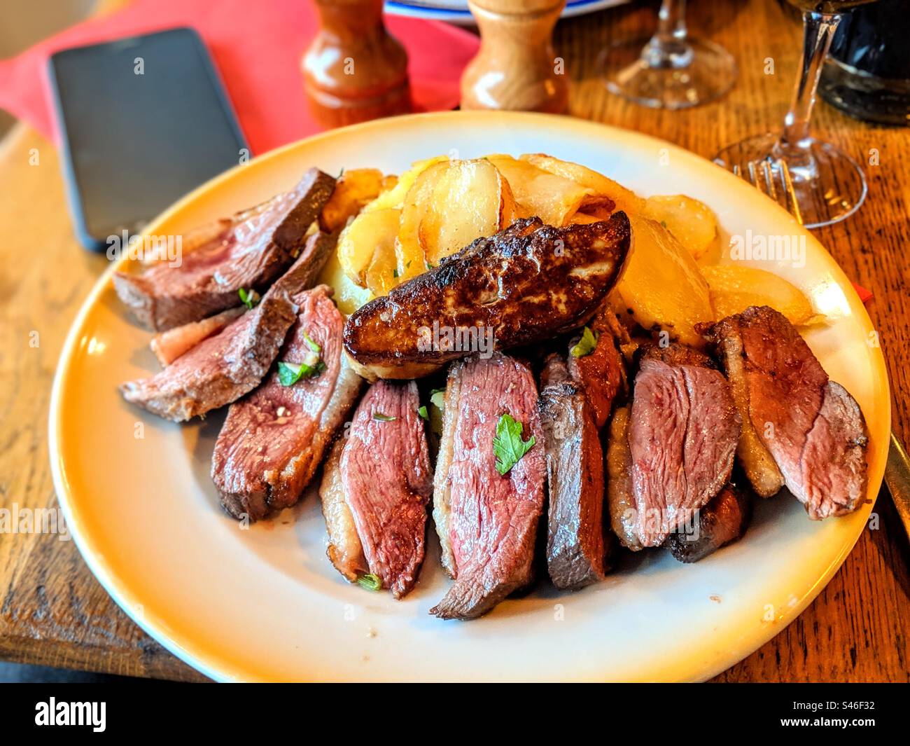 Une assiette rustique avec de la viande de canard et du foie gras et des pommes de terre dans un restaurant français sur une table, photographiée du point de vue pov Banque D'Images