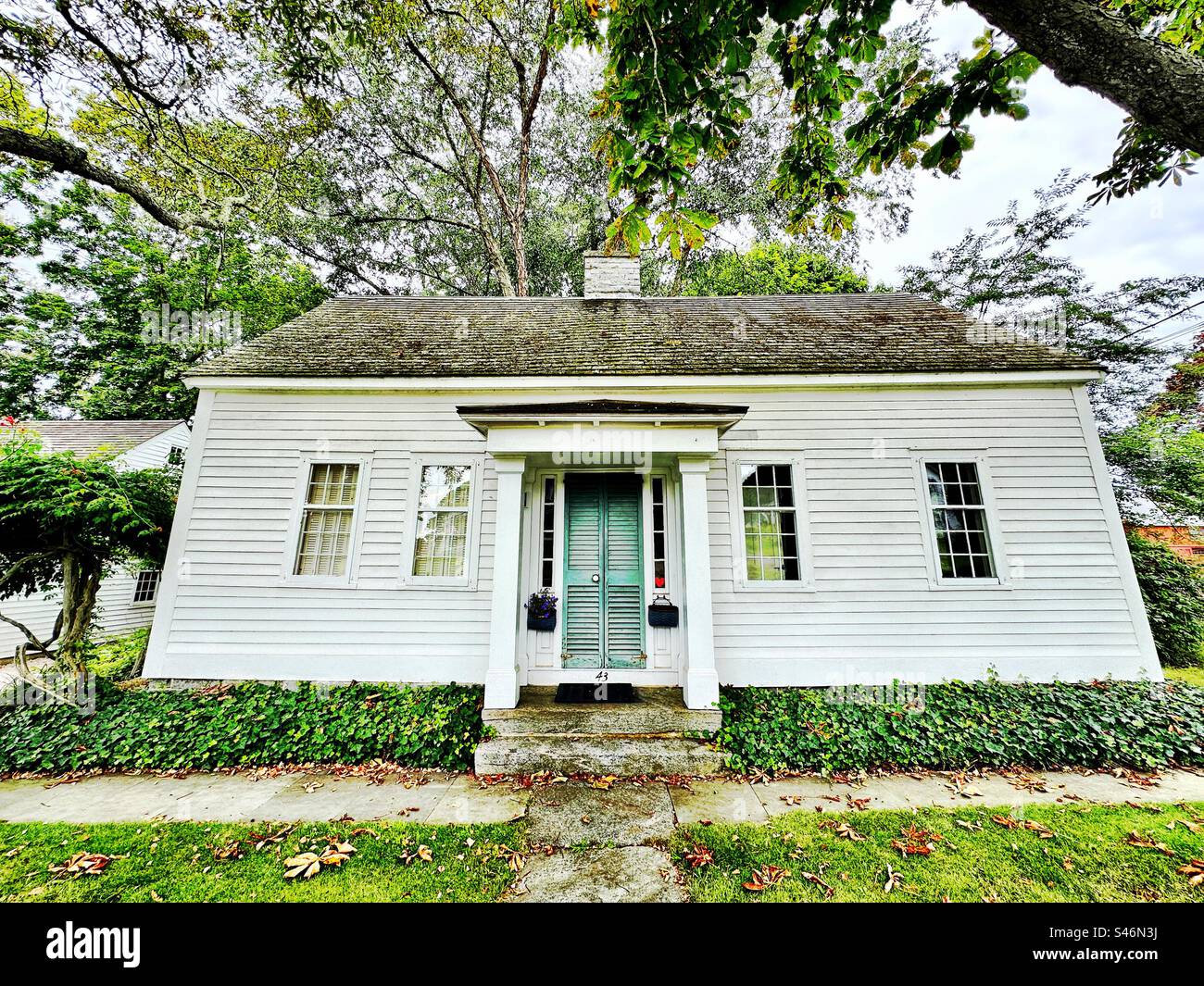 Petite, vieille, maison blanche à Clinton, Connecticut, USA. Prise avec un objectif grand angle le jour de l'été. Bâtiment vintage en Nouvelle-Angleterre. Porte d'entrée unique avec volets. - Image de stock capturée avec un smartphone