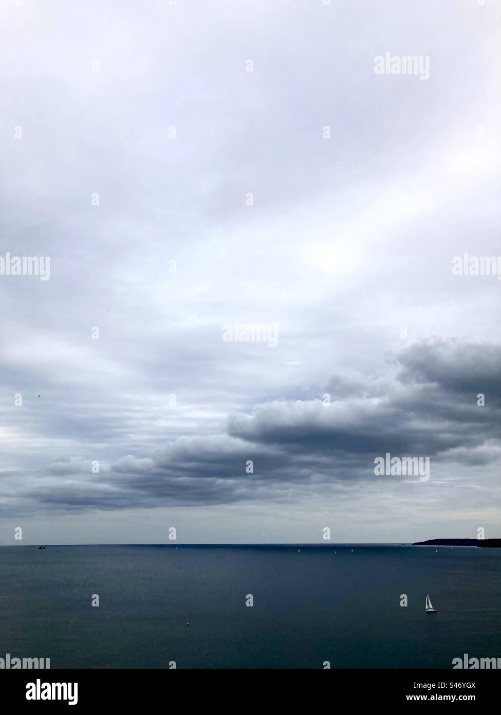 Formation inhabituelle de nuages au-dessus d'une mer sombre avec des voiles blanches si un yacht dans le coin inférieur Banque D'Images