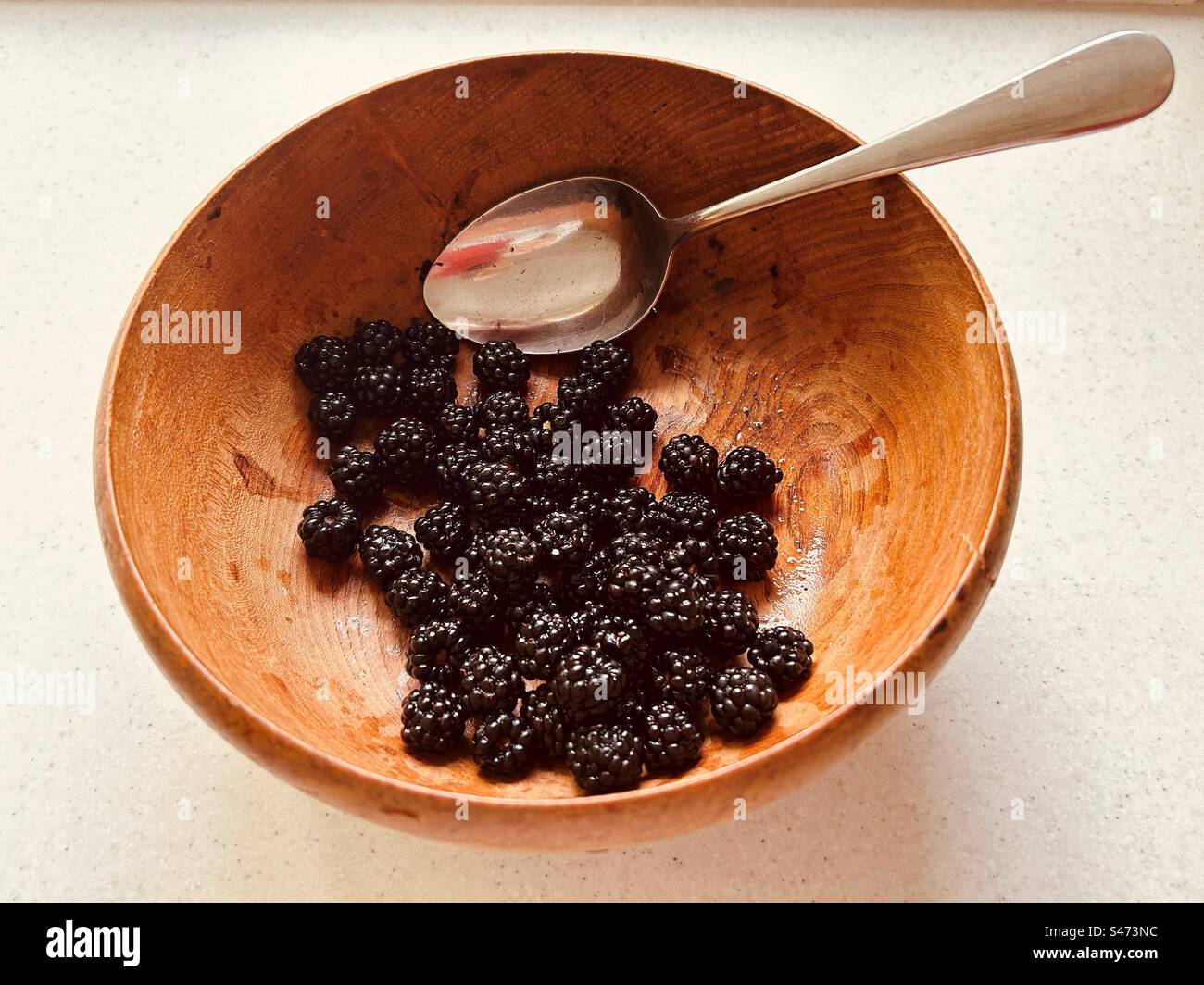 Mûres et une cuillère en acier inoxydable dans un bol en bois grainé. Fruit fourré, d'origine locale, nutritif. Banque D'Images