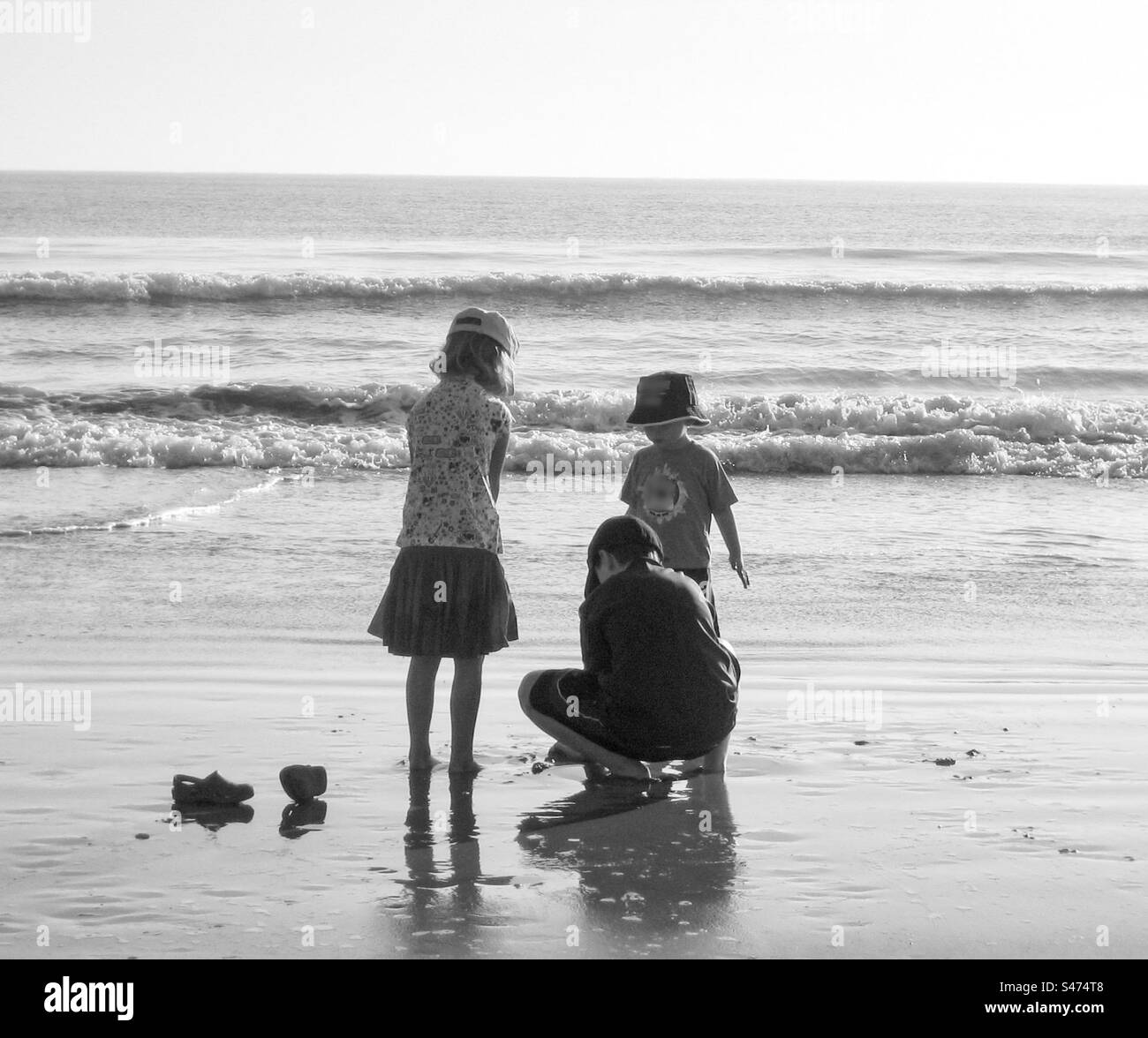 Trois enfants jouant sur une plage en noir et blanc. Banque D'Images