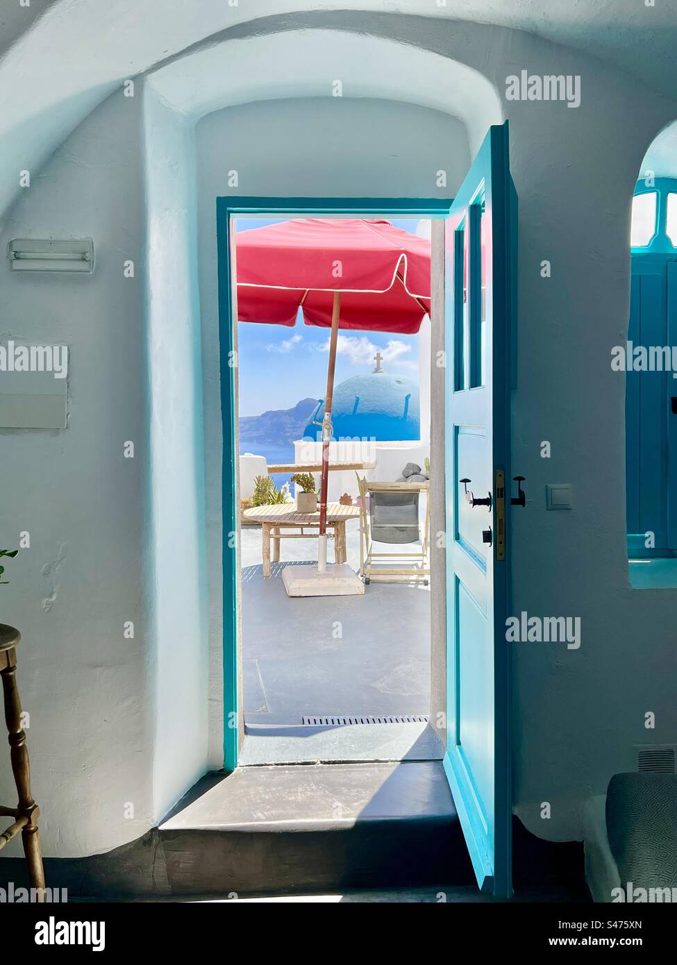 Un parapluie rouge et le dôme bleu de St. L'église de Spyridon vue à travers une porte ouverte aqua dans une suite de grotte font une vue colorée à Oia, Santorin. - Image de stock capturée avec un smartphone