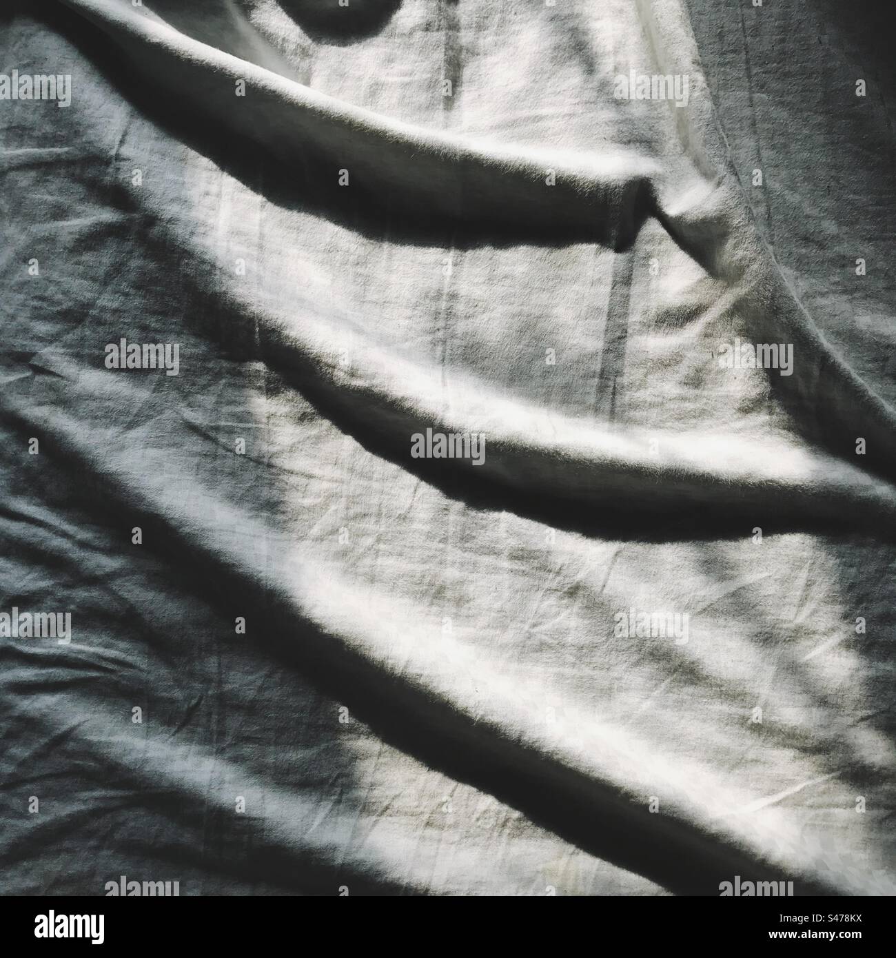 Les plis et les plis d'un drap de lit gris sur un lit dans la lumière de la fenêtre du matin Banque D'Images