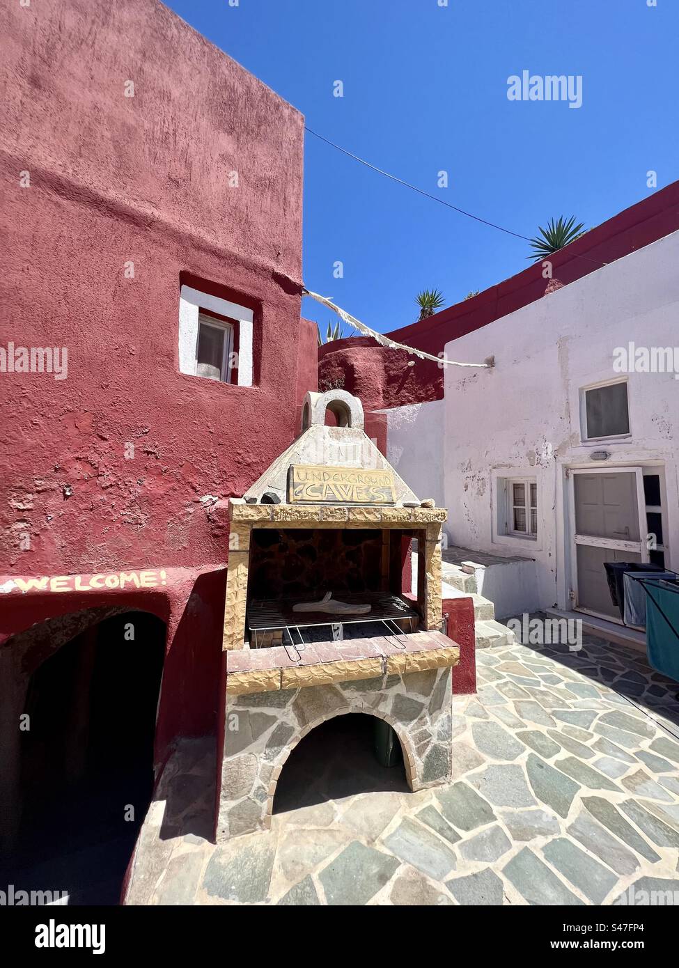 Une petite cour parmi les bâtiments à Megalochori avec un bâtiment rouge et des panneaux vous invitant à entrer dans les grottes souterraines. - Image de stock capturée avec un smartphone