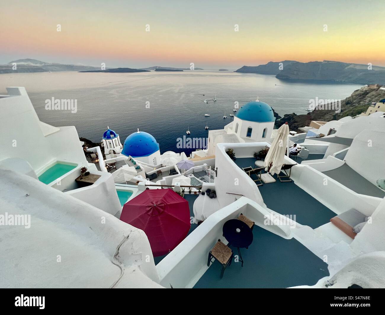 Vue sur la caldeira d'Oia, Santorin et la mer Égée au coucher du soleil avec les célèbres 3 dômes bleus en vue. - Image de stock capturée avec un smartphone