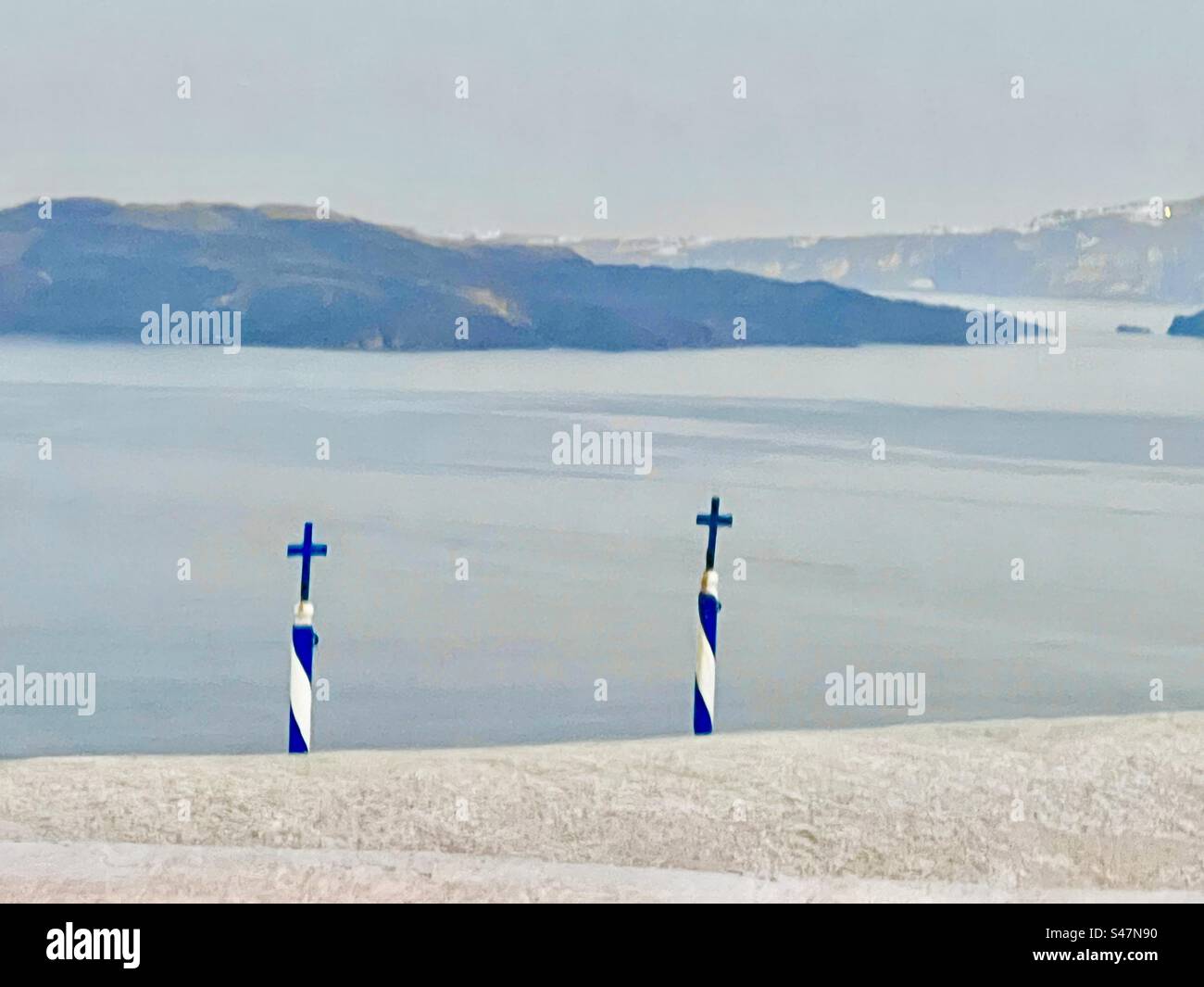 Deux poteaux rayés aux couleurs du drapeau grec, bleu et blanc, surmontés d'une croix jetant un regard sur un bâtiment blanc sur les pentes de la caldeira dans la mer Égée dans le village d'Oia, Santorin. Banque D'Images