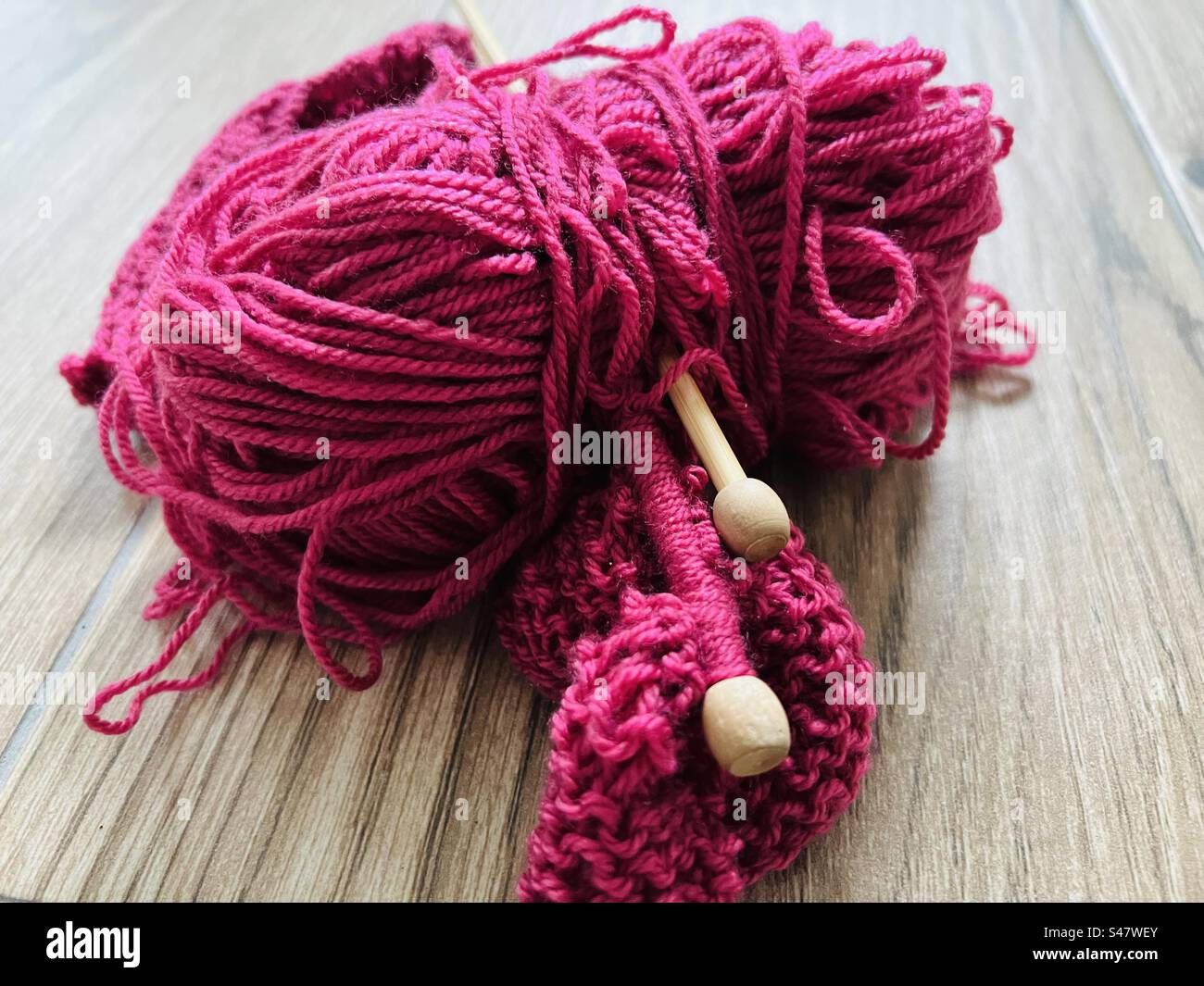 Une boule de laine rose framboise avec des aiguilles à tricoter Banque D'Images