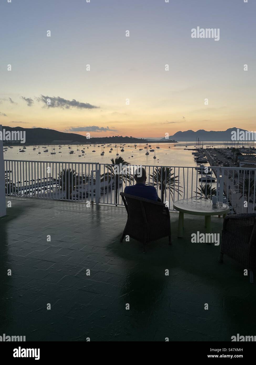 Homme profitant du lever du soleil tôt le matin à Port de Pollença, Majorque. Homme assis dans une chaise sur le toit d'un bâtiment surveillant le port à Port de Pollença. Banque D'Images