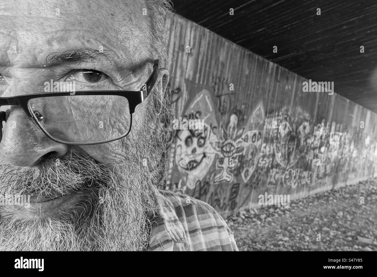 Portrait monochrome de l'homme âgé contre le mur de graffiti dans la ville Banque D'Images