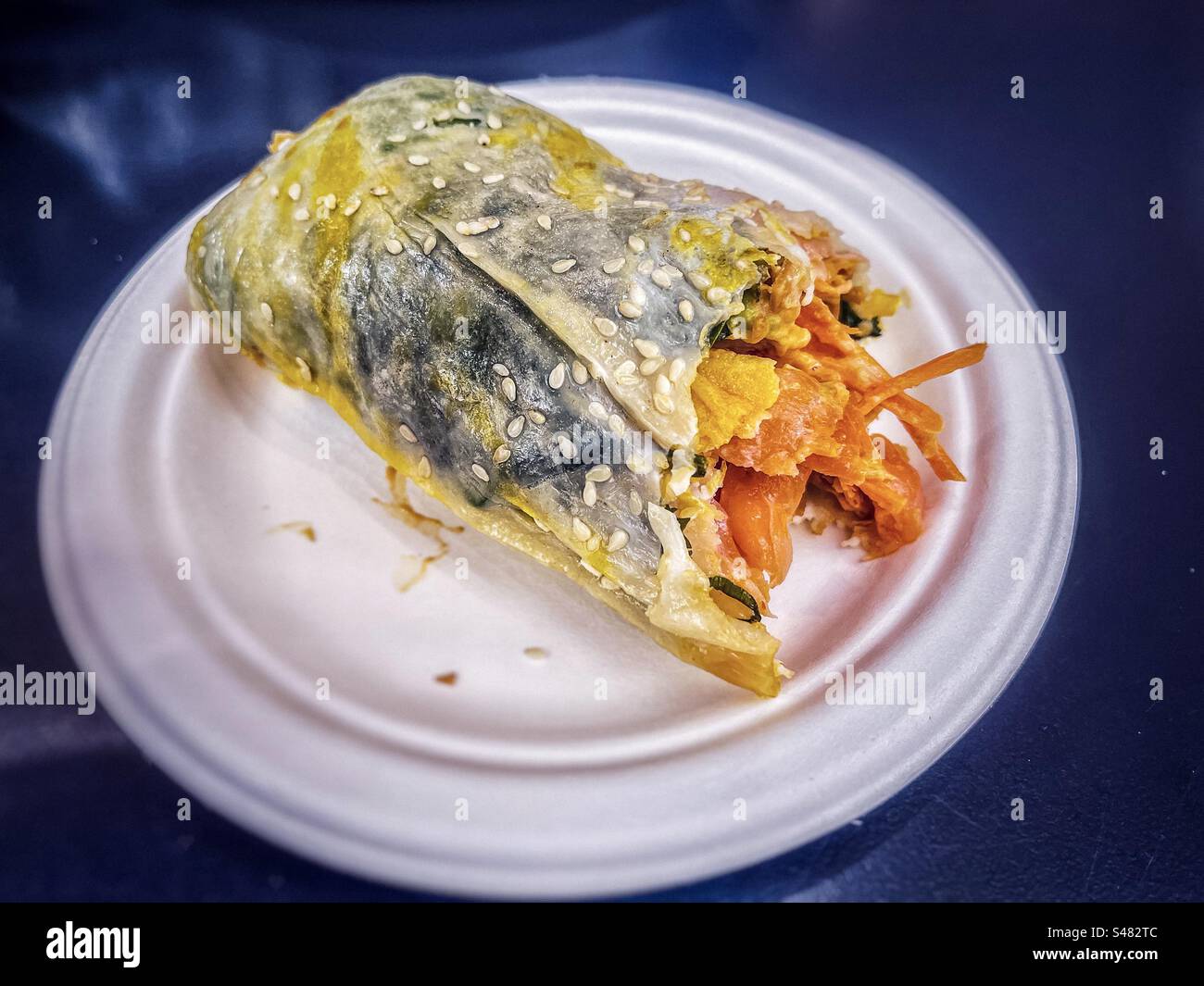 Gros plan de crêpe chinoise partiellement mangée farcie de saumon fumé, de légumes mélangés et de mayonnaise sur une assiette sur la table. Cuisine chinoise/fusion. Banque D'Images