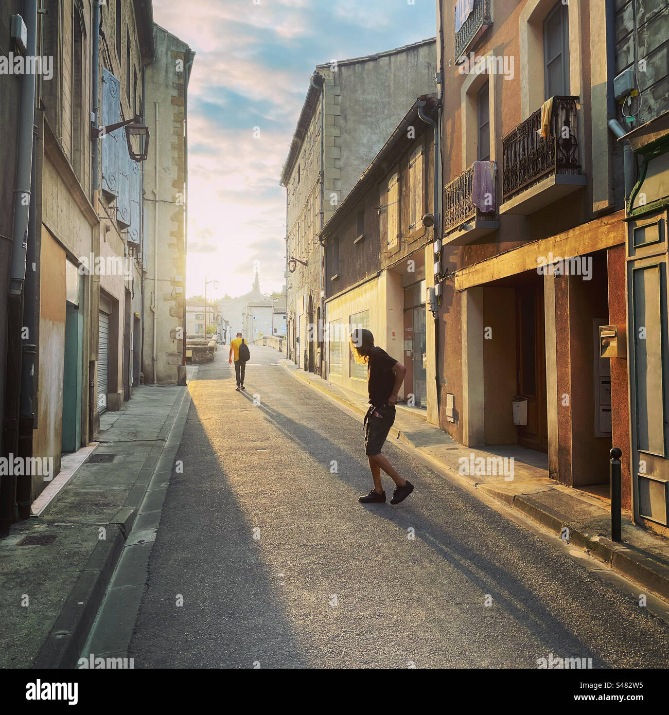 Homme quittant la maison dans la rue historique de Limoux avec une lumière douce tôt le matin dans des couleurs pastel et des ombres. Banque D'Images