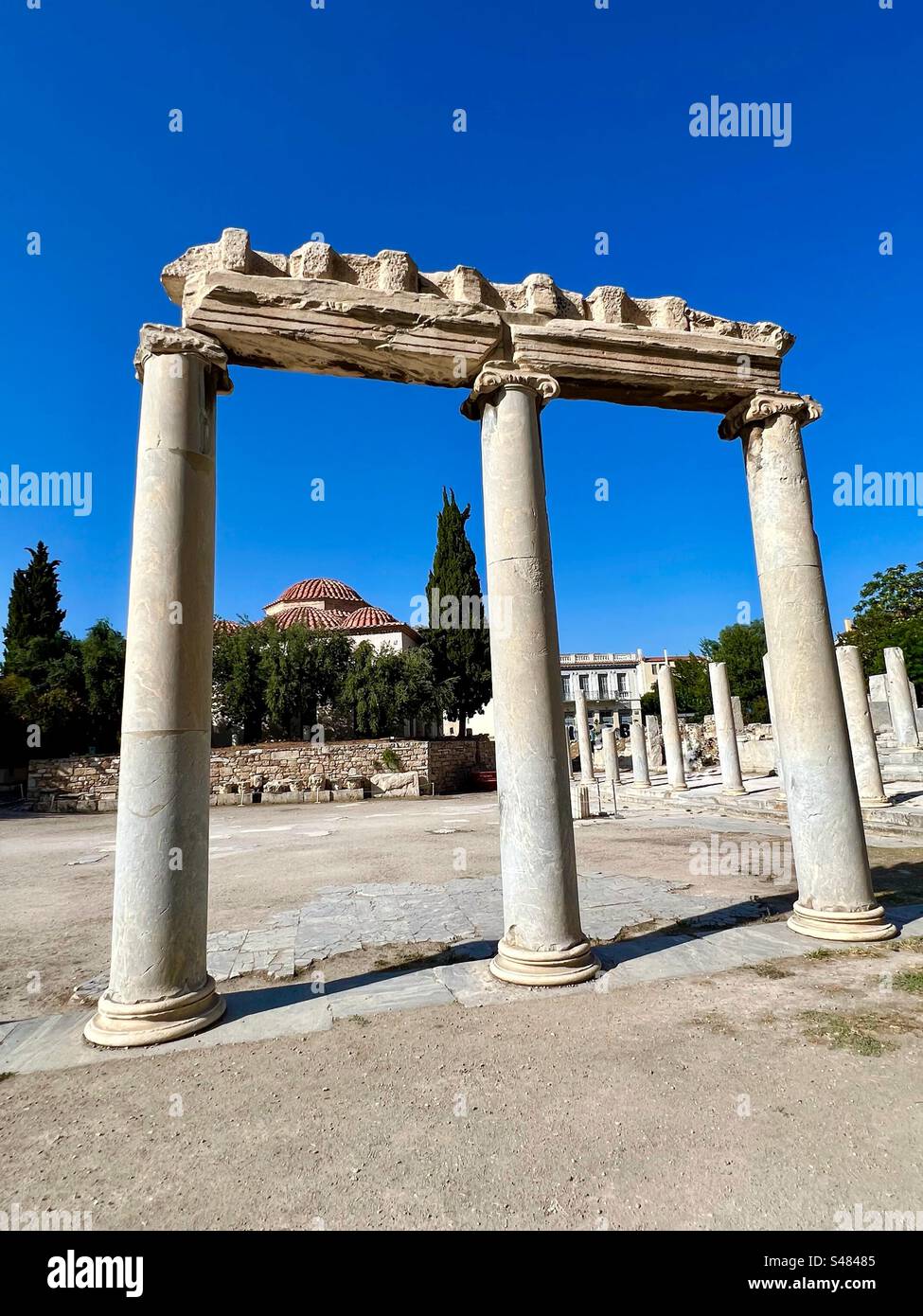 Les anciennes colonnes se dressent dans l'Agora romaine d'Athènes avec le toit en dôme de la mosquée Fethiye derrière les arbres en arrière-plan. - Image de stock capturée avec un smartphone