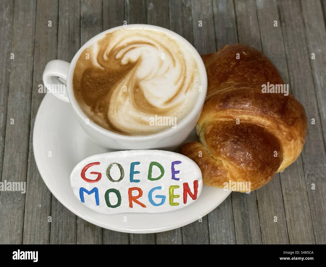 Goede morgen, bonjour en langue néerlandaise sculpté et coloré sur une pierre avec cappuccino et croissant à la table de bar Banque D'Images