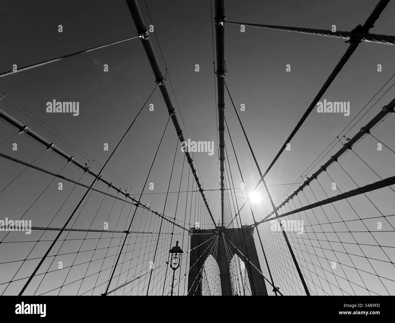 Support de voûte plantaire et câbles de suspension du pont de Brooklyn en silhouette contre le soleil. Avec la lampe et le soleil lumineux rétro-éclairant le motif des câbles de suspension Banque D'Images