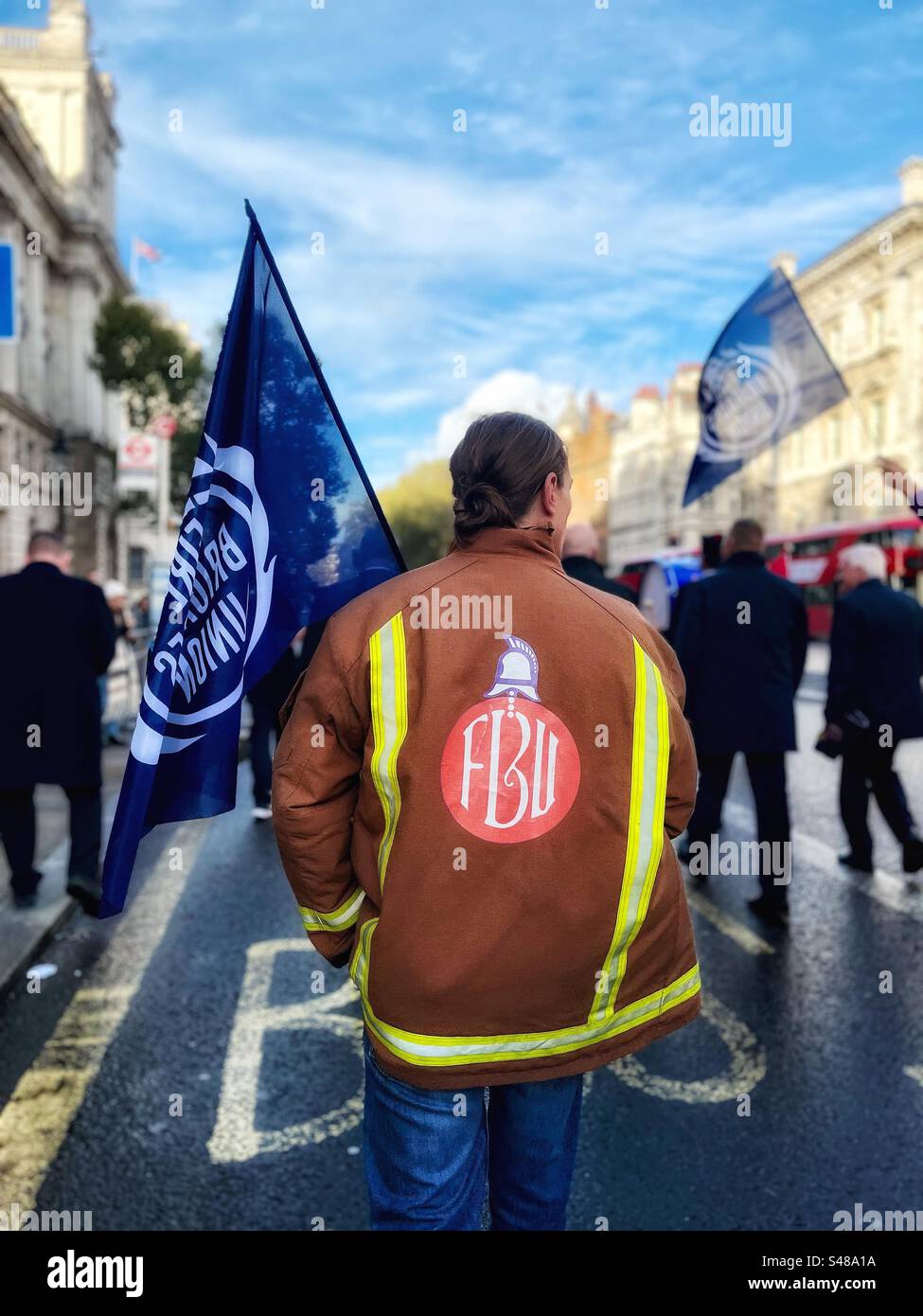 Un pompier avec une veste logo FBU - lors d'une manifestation à Westminster, Londres le 1 novembre 2023 tient drapeau. La FBU est un syndicat représentant les travailleurs des services d'incendie à travers le Royaume-Uni Banque D'Images