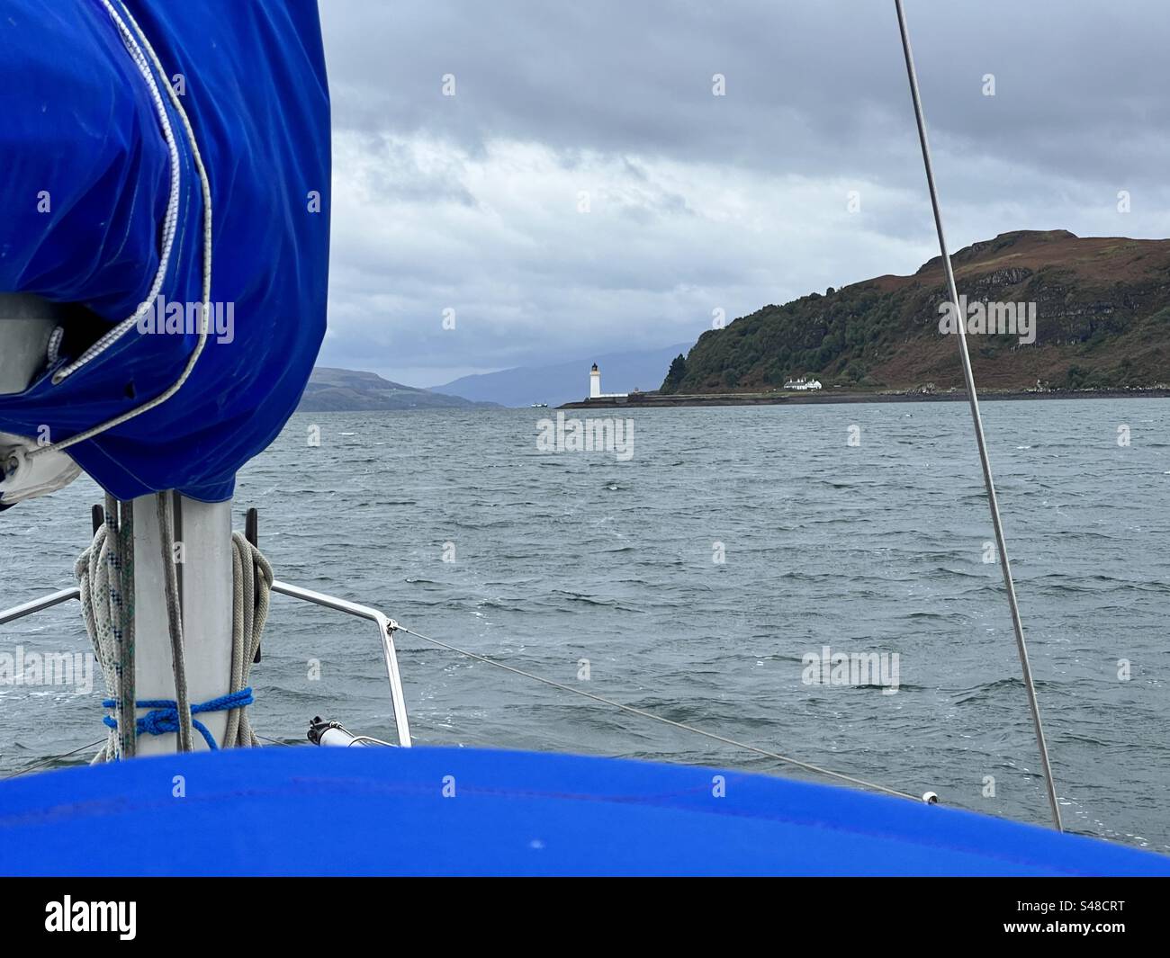 Une image d'un phare éloigné prise d'un voilier, avec des parties bleues du bateau (toile couvrant la voile et bimini) et la mer visibles. Banque D'Images