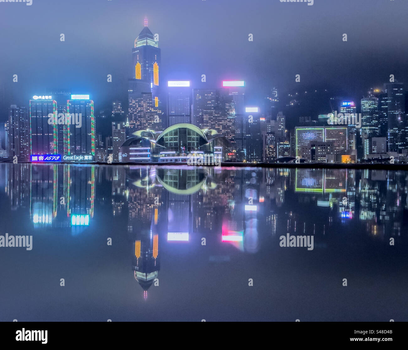Horizon de Hong Kong par une nuit pluvieuse, reflétée sur la surface humide le long de la promenade dans le port de Victoria Banque D'Images