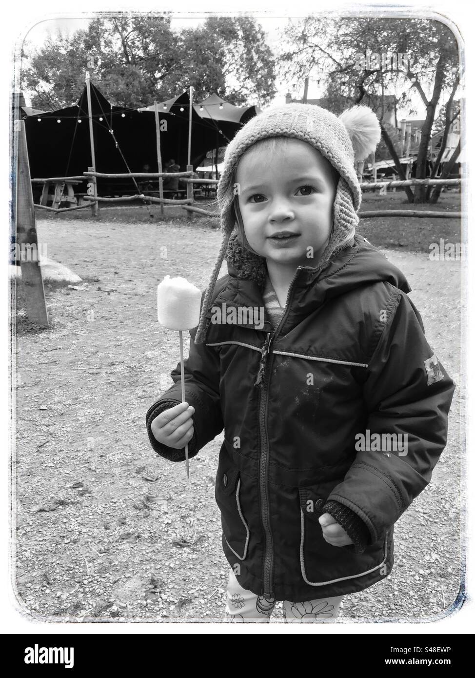 Enfant en chapeau et manteau tenant une guimauve sur un bâton mono noir et blanc automne Banque D'Images