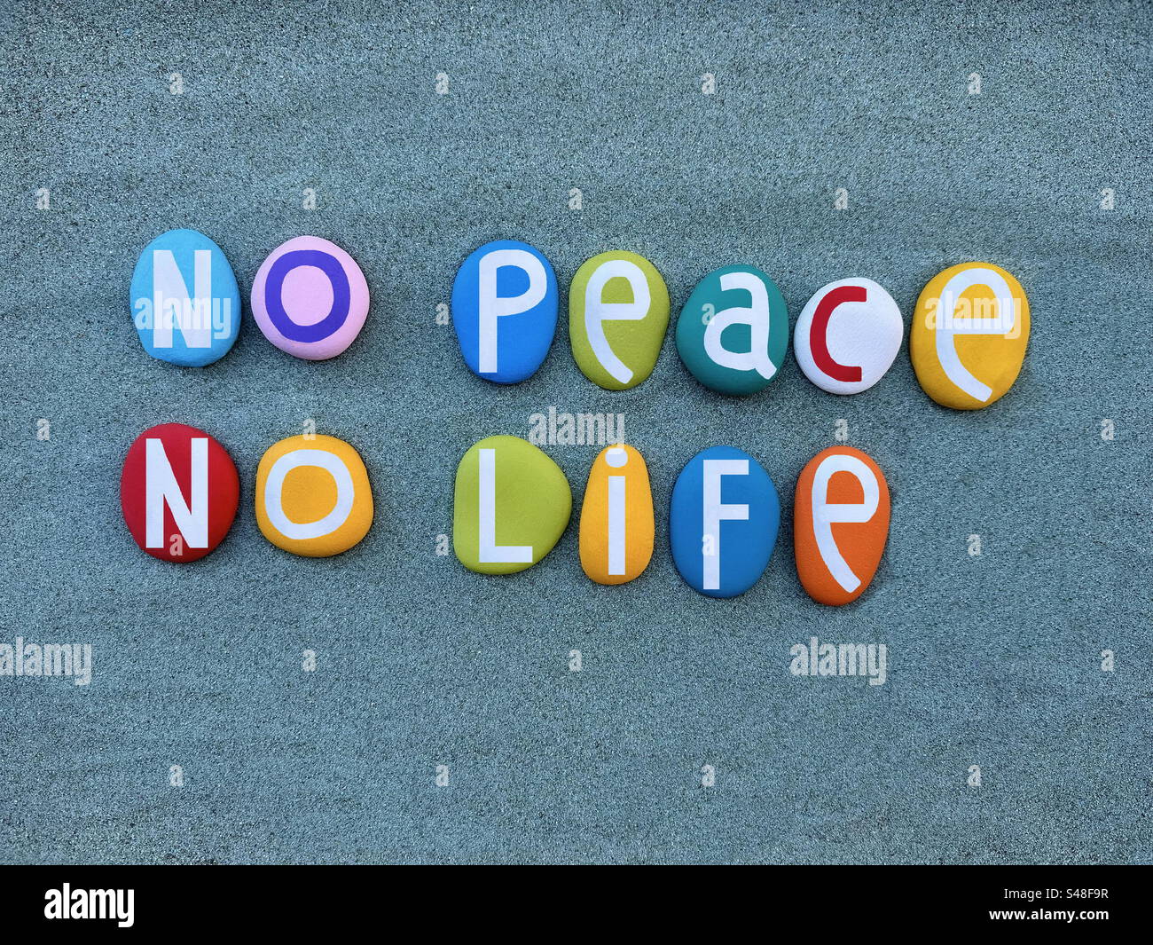 No Peace, no Life, slogan créatif composé de lettres de pierre multicolores peintes à la main sur du sable vert Banque D'Images