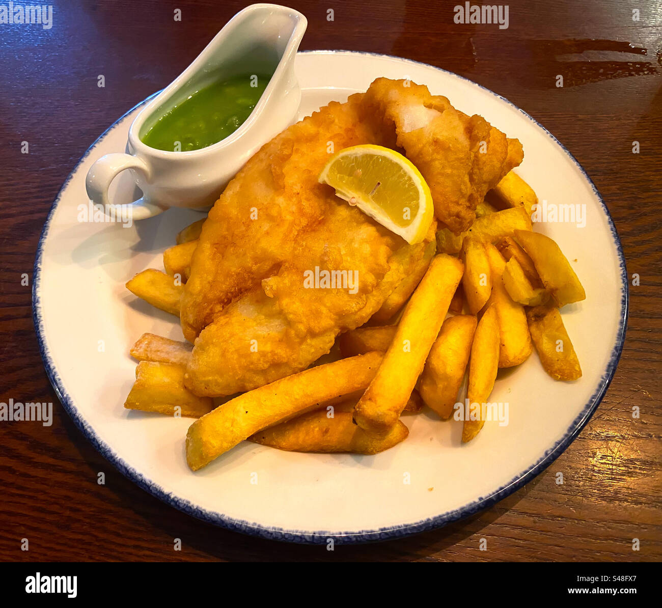 Fish and chips avec une cruche de pois pâteux pour linch dans un pub. Banque D'Images