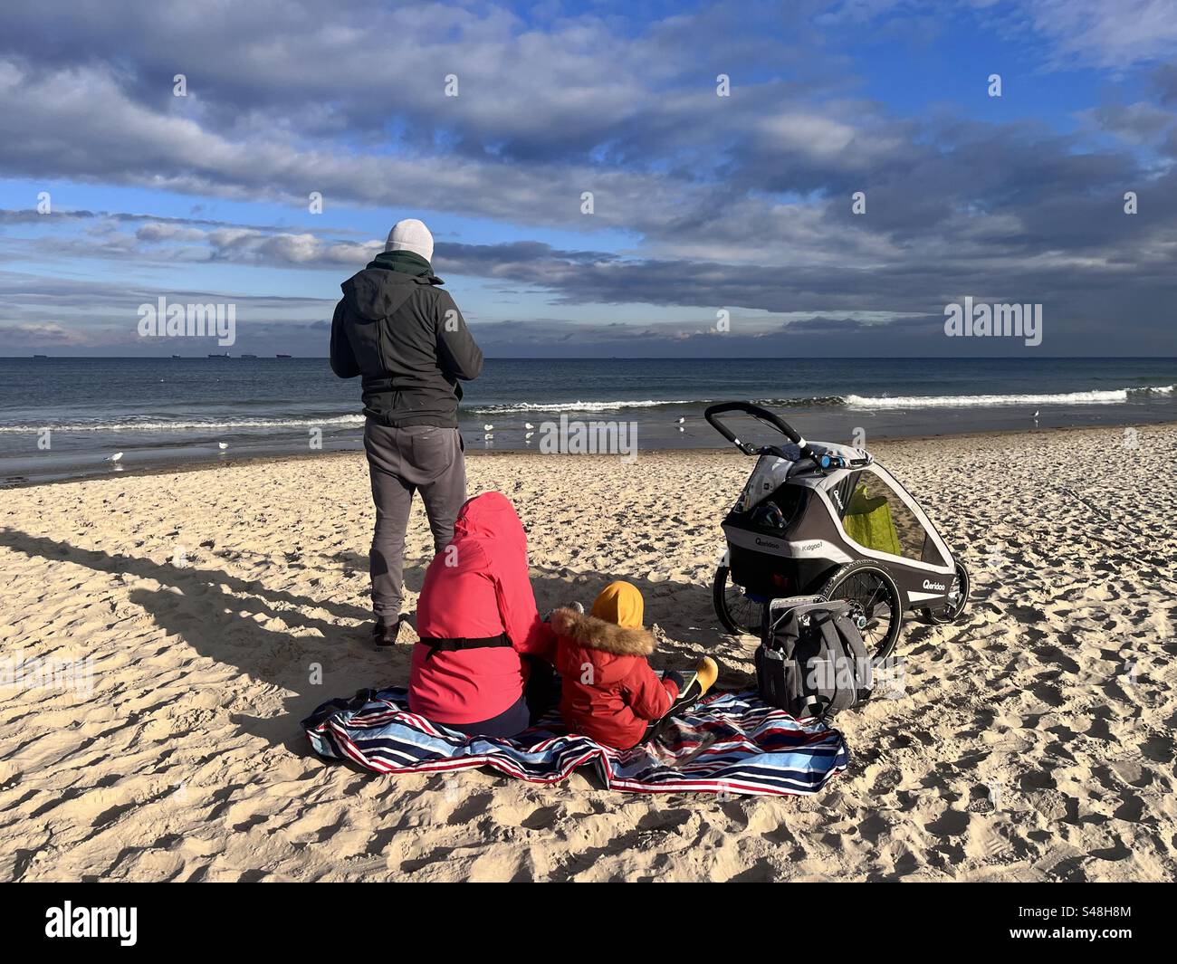 Famille portant des vestes sur la plage de sable avec le ciel sombre le jour ensoleillé d'hiver. Plage de Przymorze, Gdansk Pologne, Europe, UE Banque D'Images