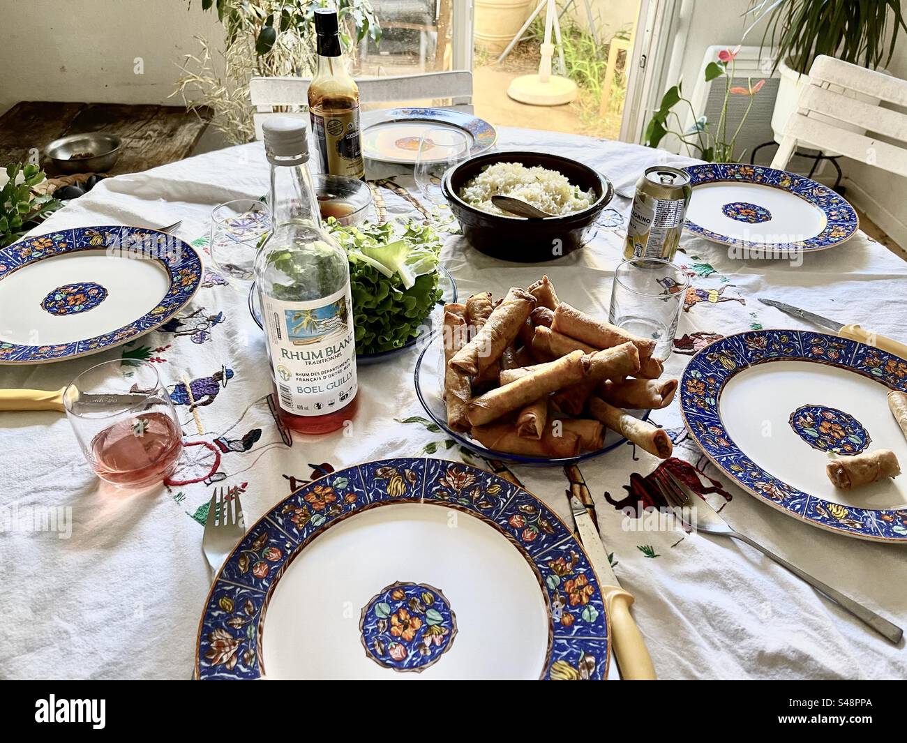 Photo d'une table à déjeuner entièrement aménagée avec assiettes décorées bleues complexes, vin français, riz blanc, rouleaux de printemps - Image de stock capturée avec un smartphone