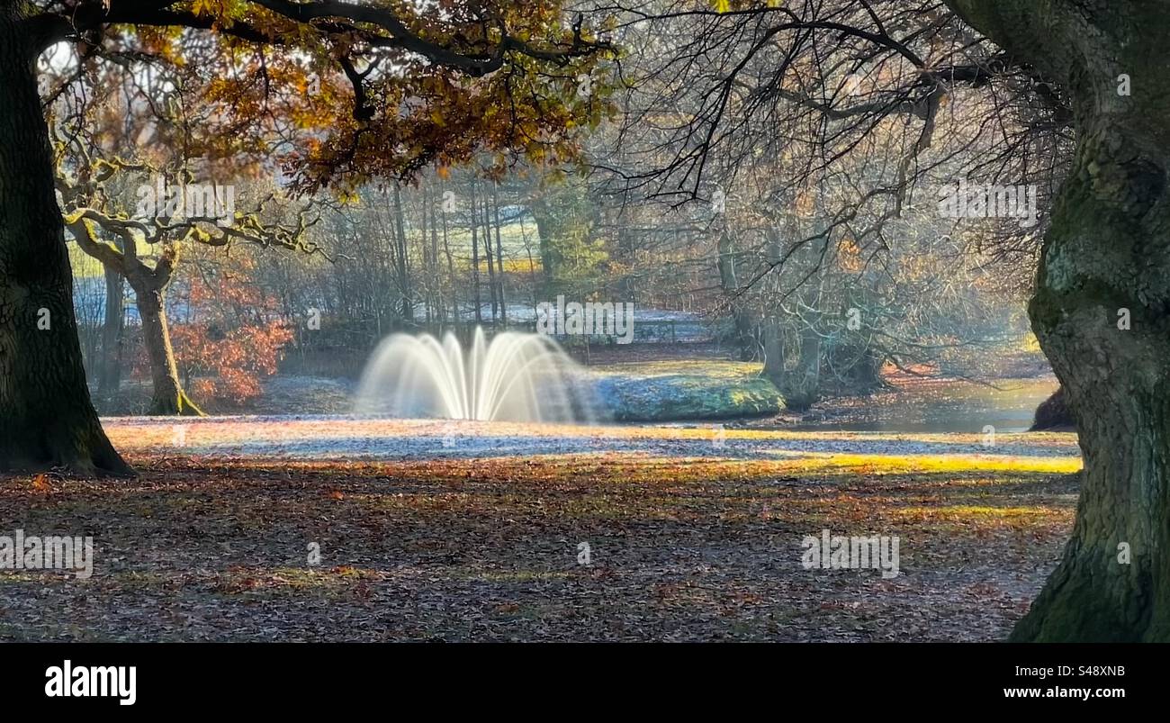 Fontaine au lac à Astley Park, Chorley sur un froid matin d'hiver avec du gel sur le sol. Restes de feuilles d'automne sur le sol. Banque D'Images