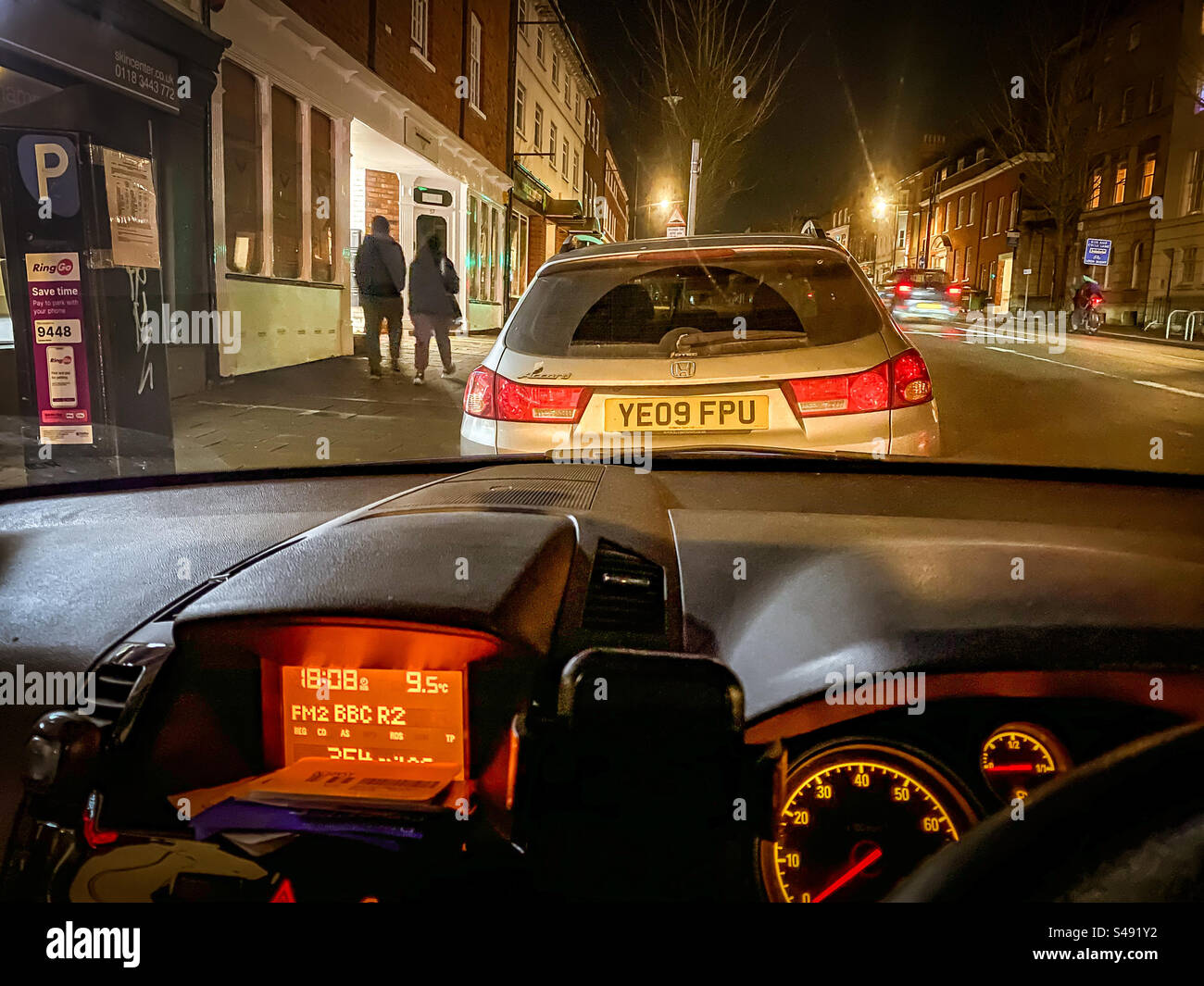 Assis dans une voiture garée, écoutant la radio. En attendant de venir chercher quelqu'un la nuit. Banque D'Images