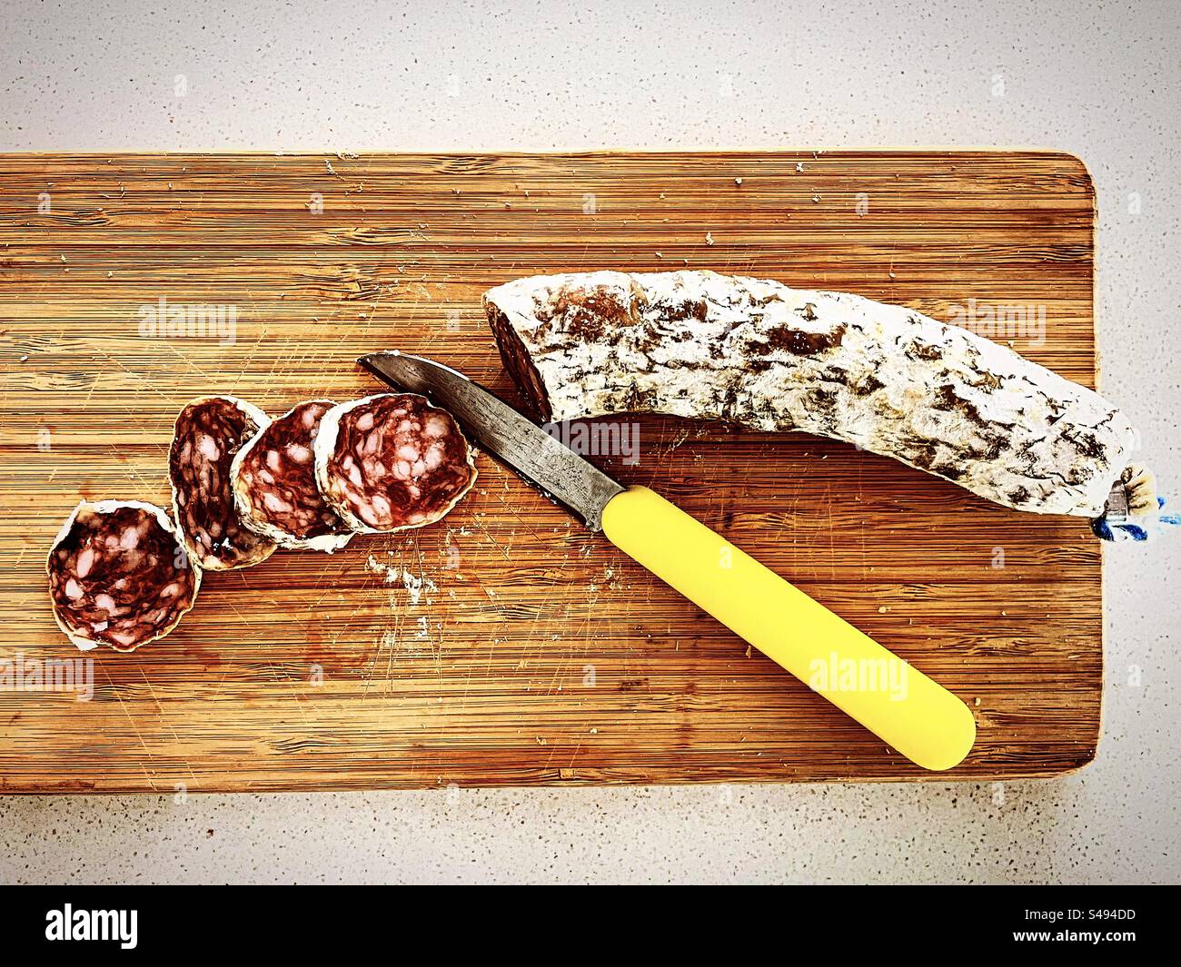 tranches de salami saucisse salée sèche saucisson de nourriture sur planche de bois avec un couteau jaune dans la cuisine prêt à être mangé manger Banque D'Images