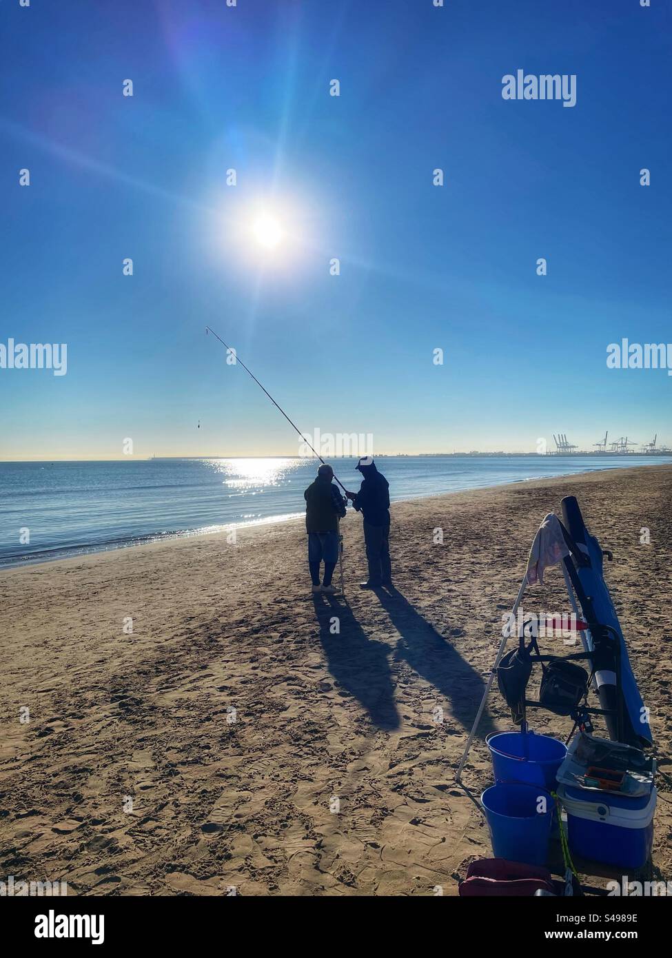 Deux hommes préparent une canne à pêche sur une plage de sable fin à Valence, en Espagne, par une douce journée ensoleillée d'hiver en décembre Banque D'Images