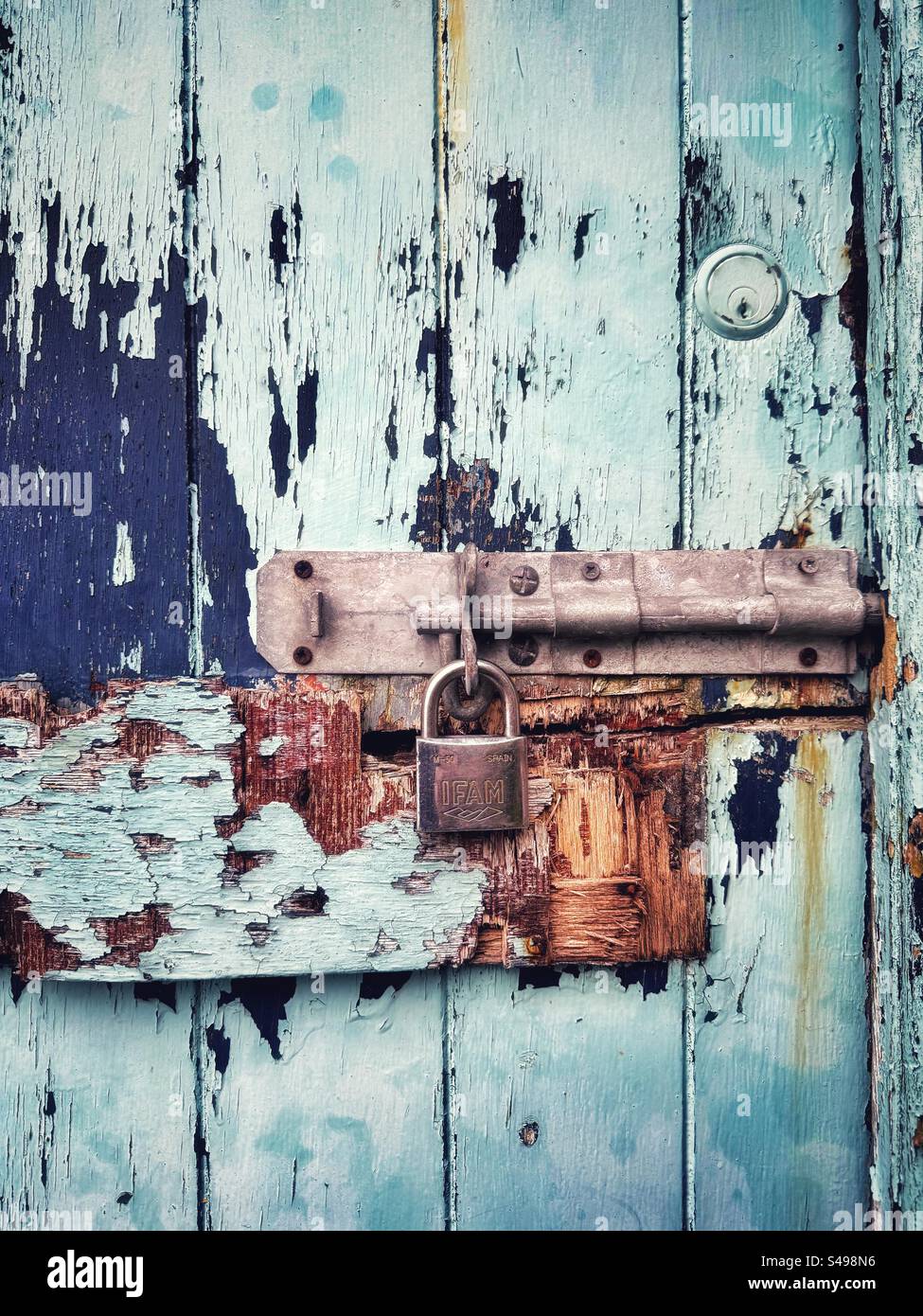 Vieille serrure sur une porte en bois battue et patinée avec écaillage et peinture délavée. Banque D'Images