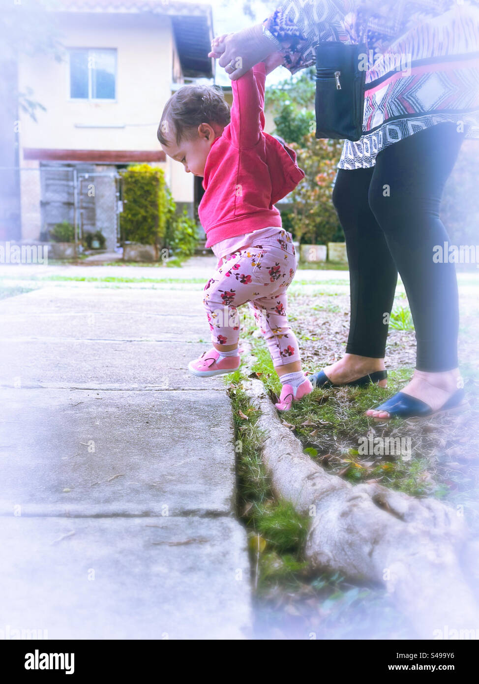 Les premiers pas de bébé à l’extérieur. Bébé marchant avec excitation étant aidé par un adulte Banque D'Images